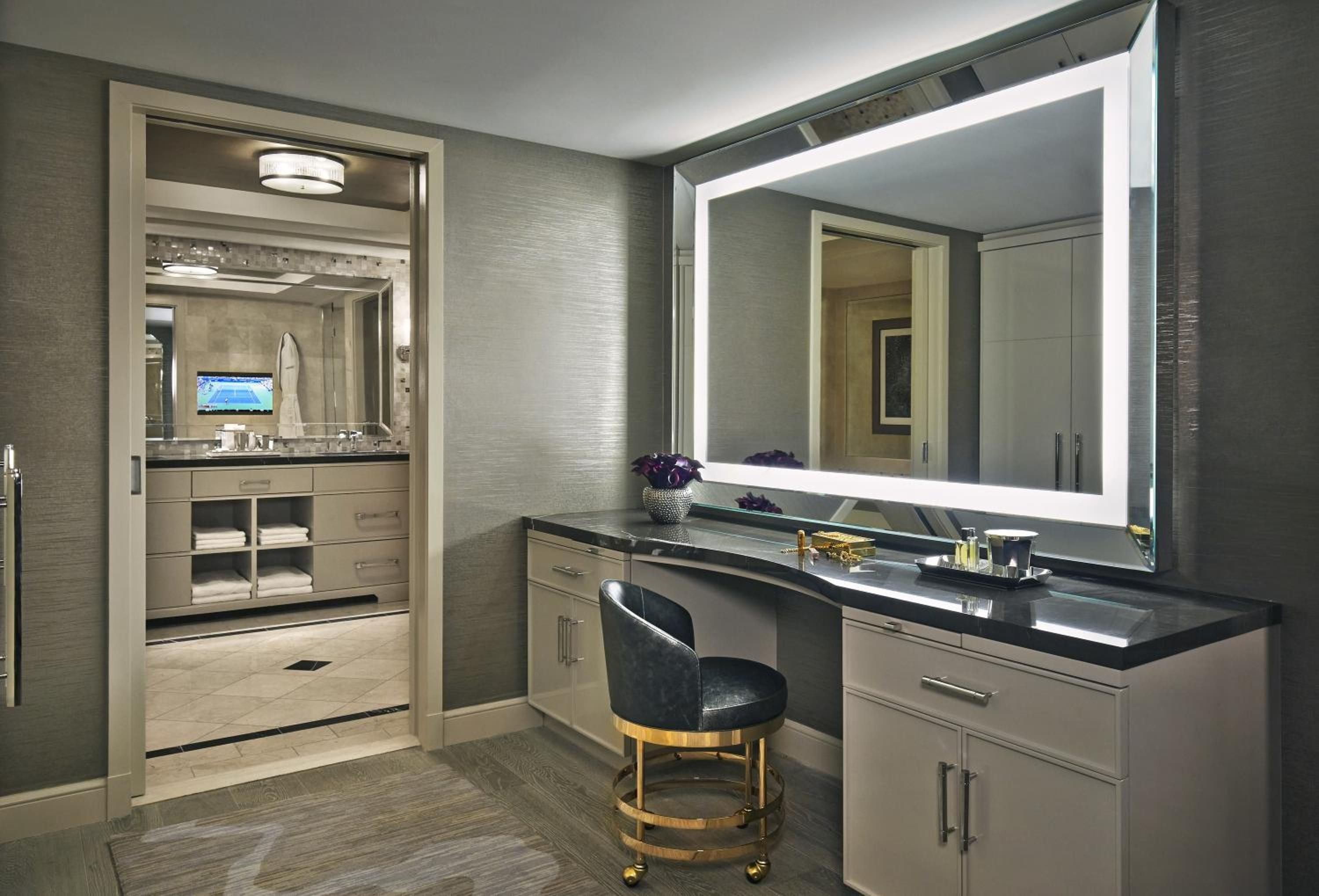Polished marble surfaces and backlit mirrors create a spa-like sanctuary where brass accents and plush seating transform daily routines into luxurious rituals.