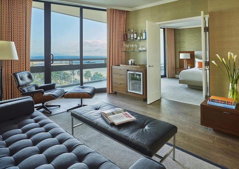 Floor-to-ceiling windows frame Pacific views from this sophisticated suite, where tufted leather seating and warm wood tones create an inviting retreat above Santa Monica's coastline.