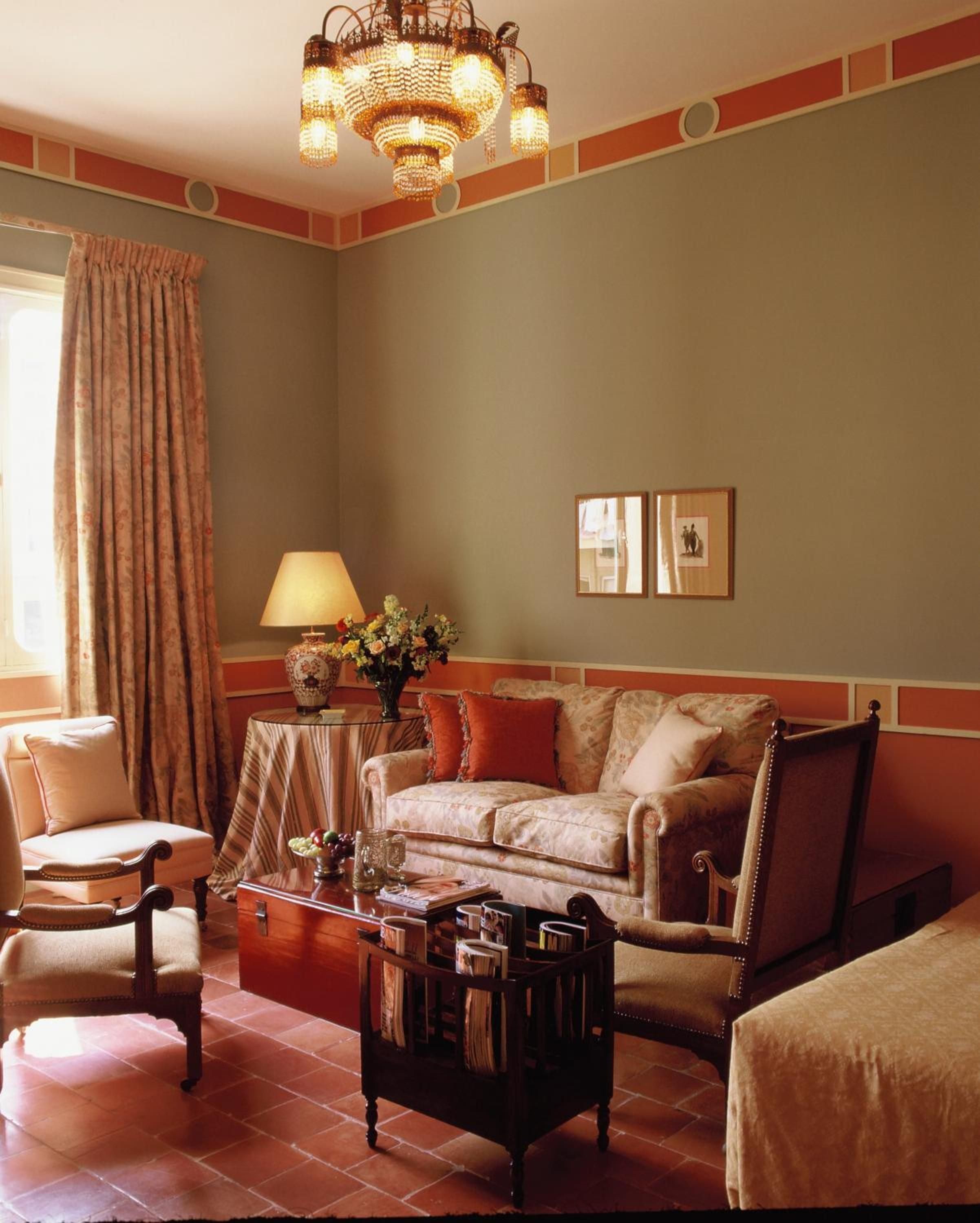 Warm terracotta tiles and sage walls create an intimate sitting area where crystal chandeliers cast golden light over plush velvet furnishings and carefully curated antiques.