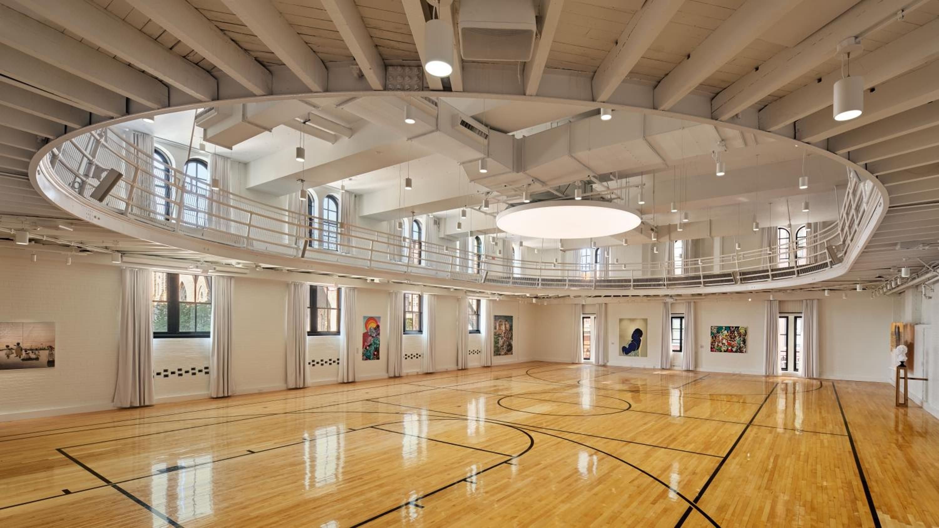 A former jail's circular cellblock transforms into an unexpected basketball court, where contemporary art adorns historic stone walls beneath soaring industrial beams and gleaming hardwood floors.