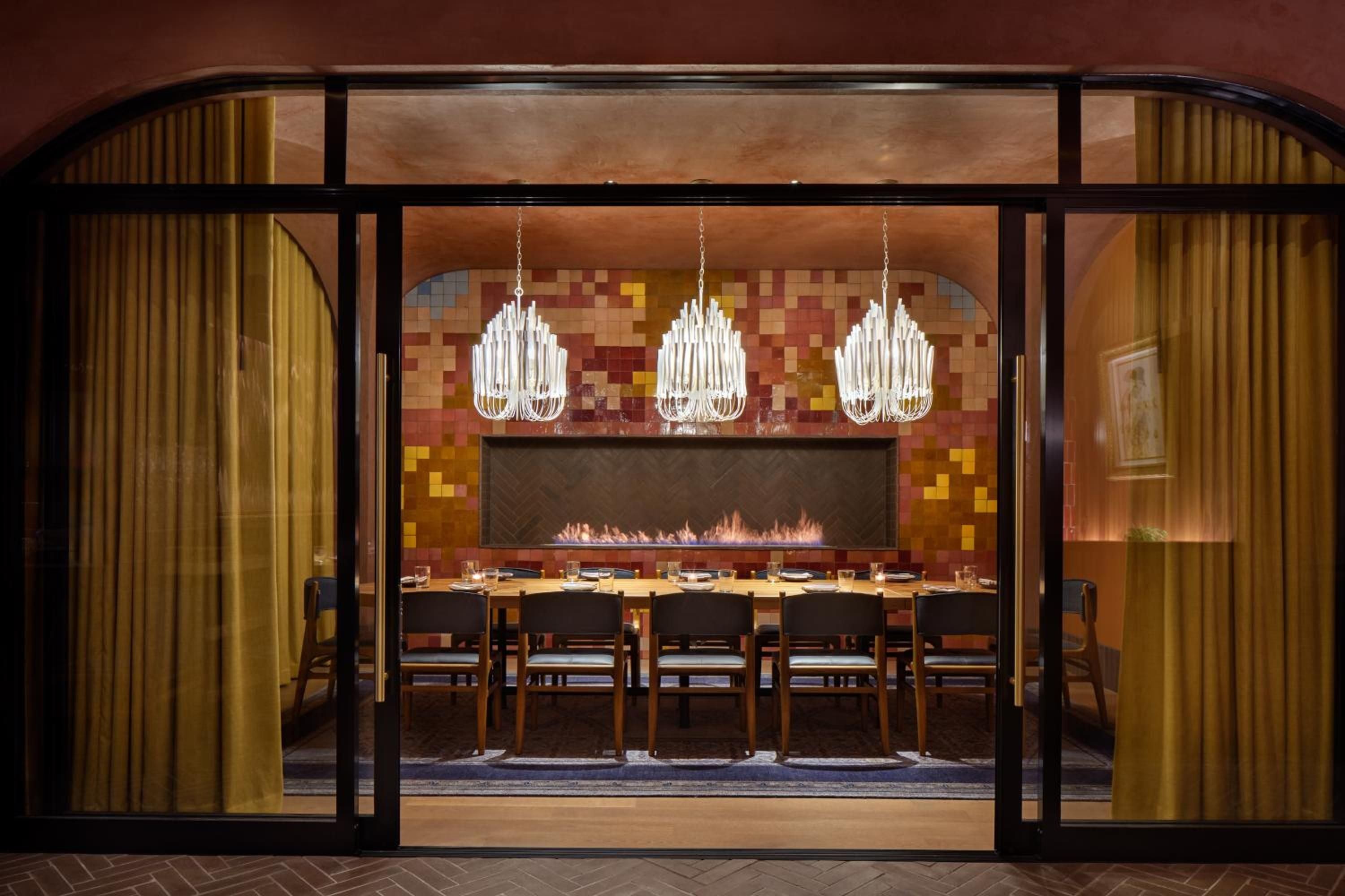 Suspended pendant lights cast warm shadows over the intimate dining room, where a mosaic tile fireplace anchors conversations around the communal table.