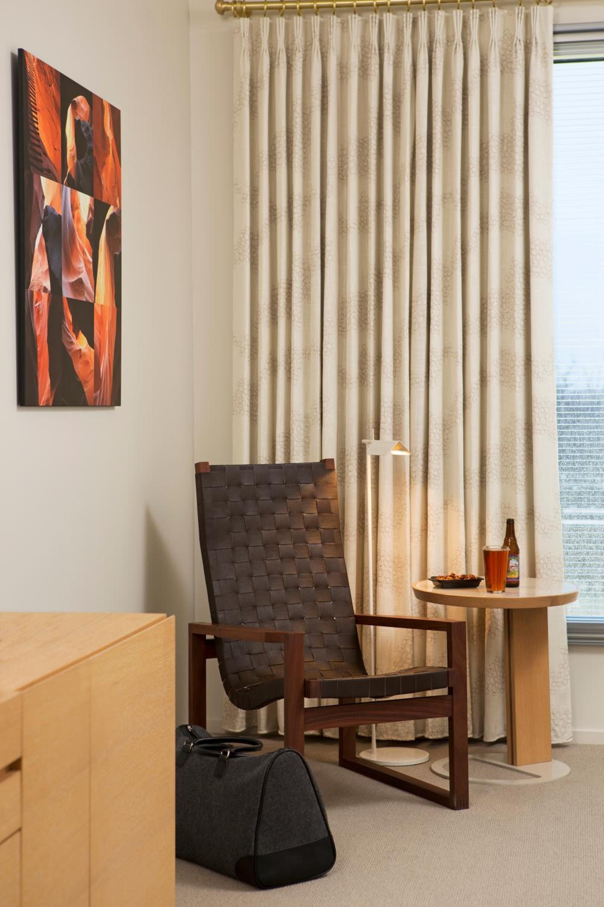 Woven leather seating and warm wood tones create an intimate corner where contemporary art meets mid-century modern comfort in thoughtfully appointed guest quarters.