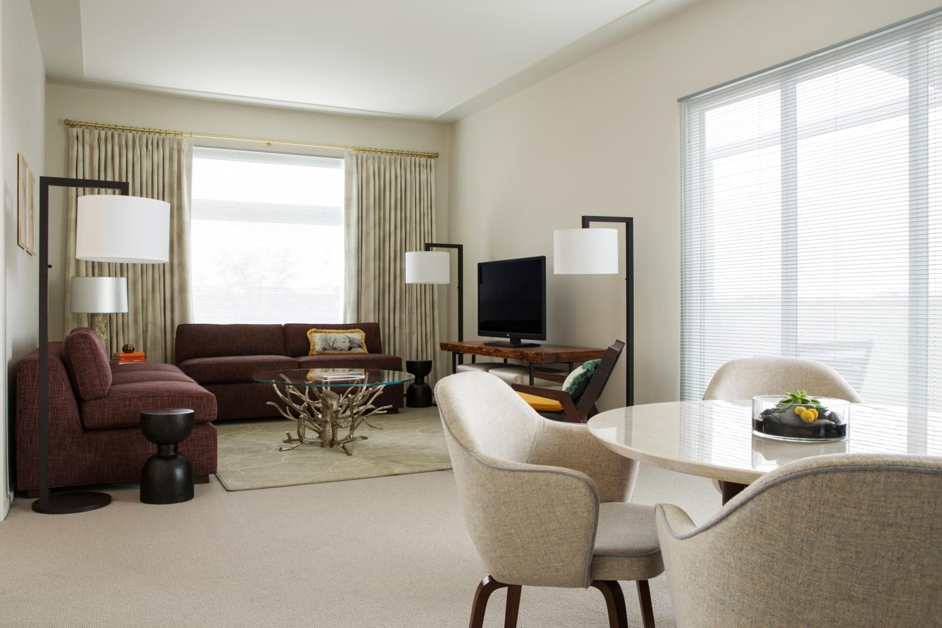 Warm afternoon light filters through floor-to-ceiling windows, illuminating the burgundy sectional and sculptural coffee table in this spacious corner suite's living area.