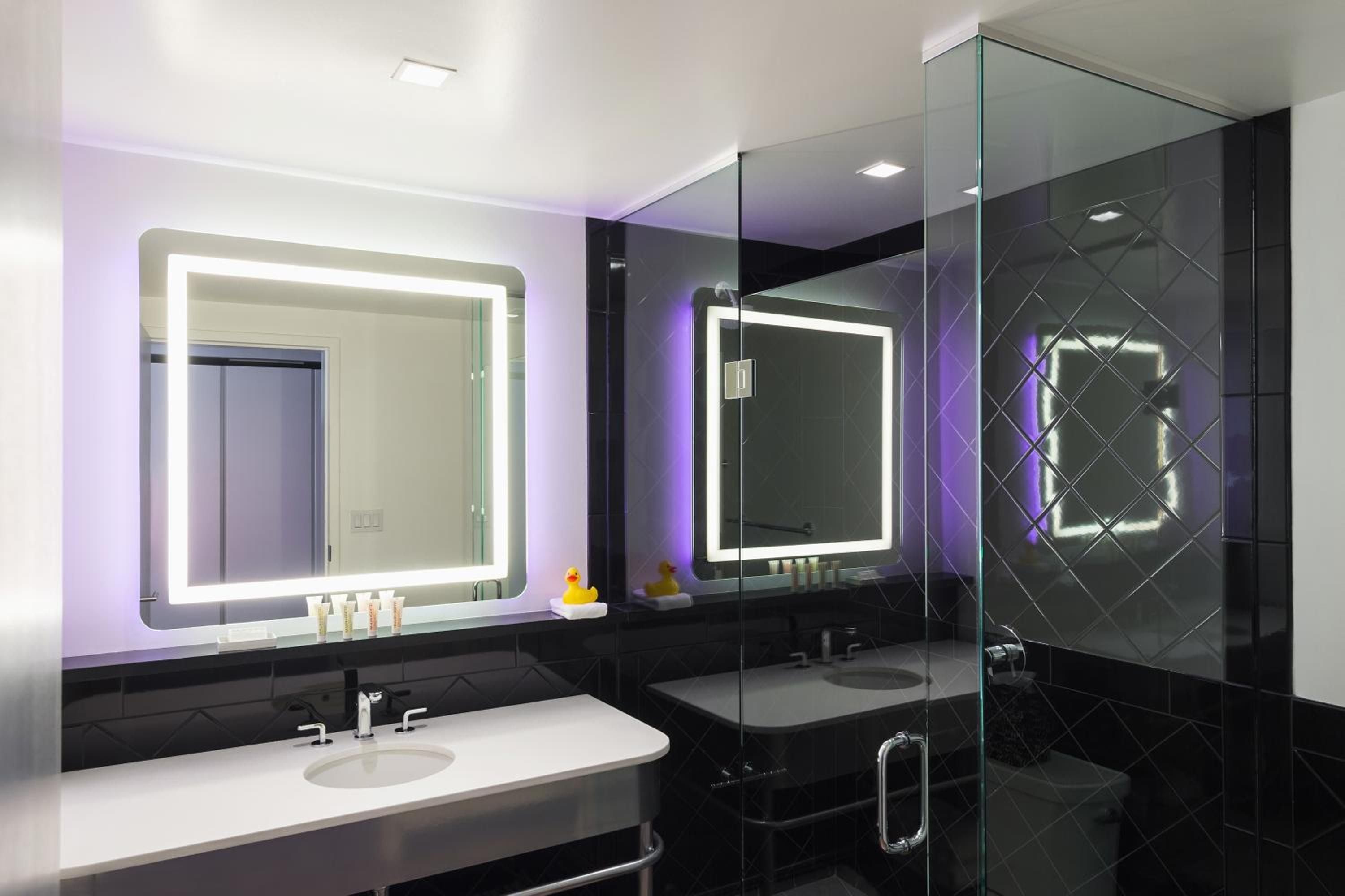 Purple ambient lighting transforms the sleek bathroom into a contemporary sanctuary, where illuminated mirrors and geometric black tiles create striking modern drama.