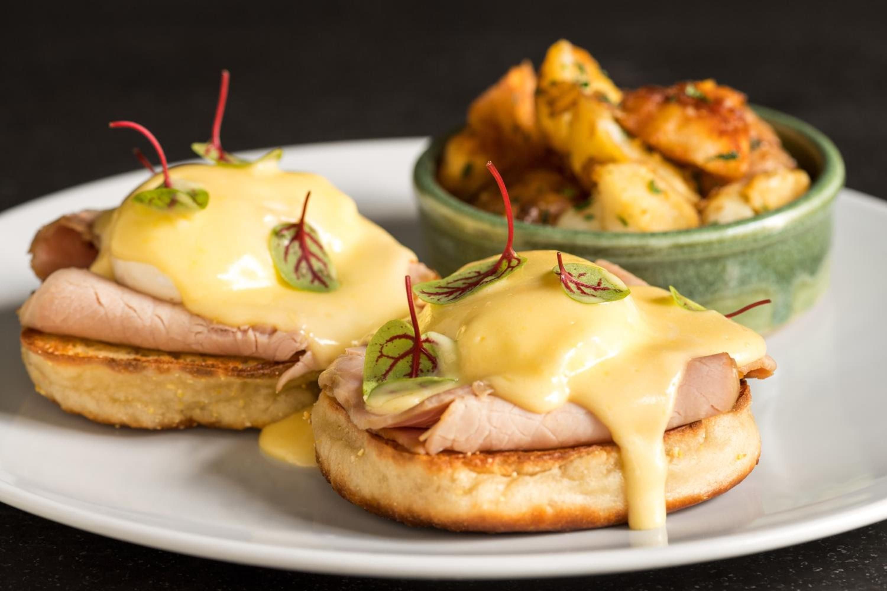 Golden hollandaise cascades over perfectly poached eggs and ham at Counting House, where classic eggs Benedict meets contemporary plating and vibrant microgreens.