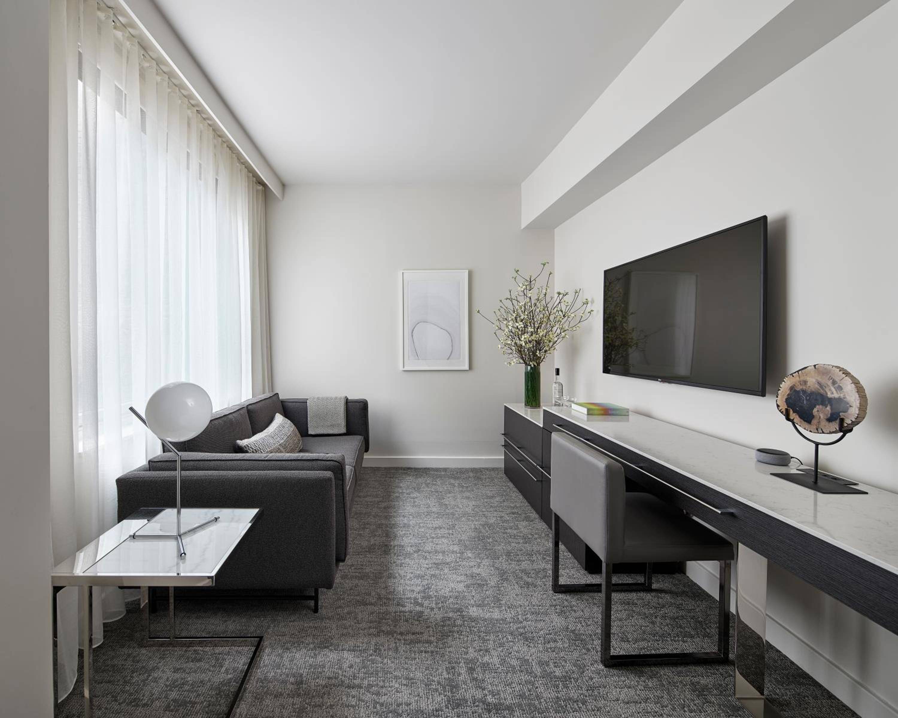 Sleek walnut cabinetry and charcoal furnishings create sophisticated contrast against crisp white walls, while floor-to-ceiling windows bathe the modern suite in natural light.