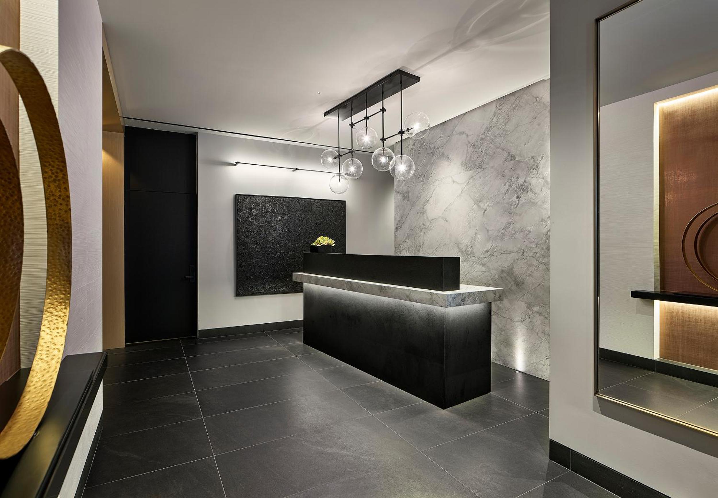 Sleek marble surfaces and warm bronze accents create an intimate check-in experience, while contemporary pendant lights cast a sophisticated glow across polished stone floors.