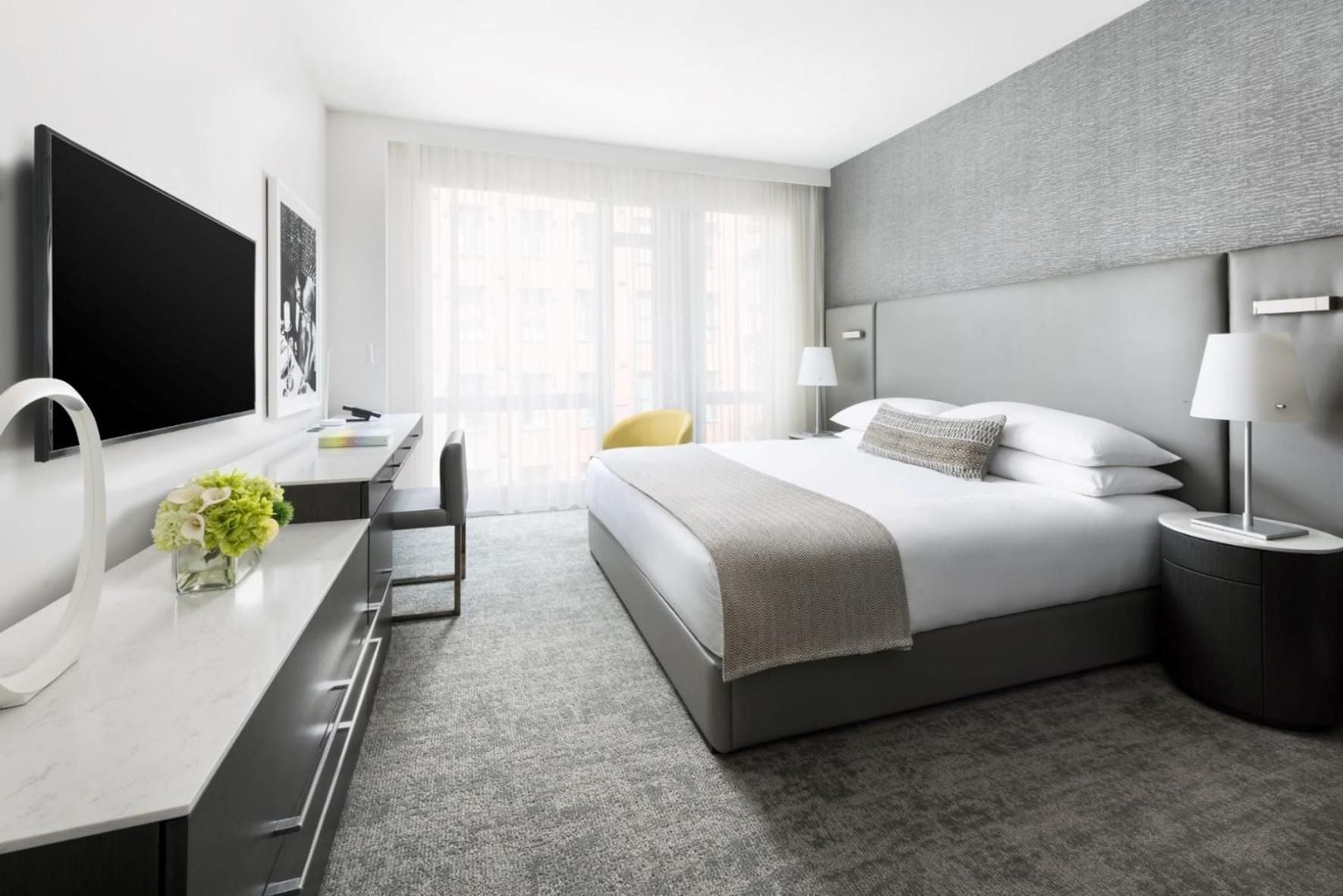 Crisp white linens meet charcoal textures in this thoughtfully appointed guest room, where natural light filters through sheer curtains and yellow accent chairs add unexpected warmth.