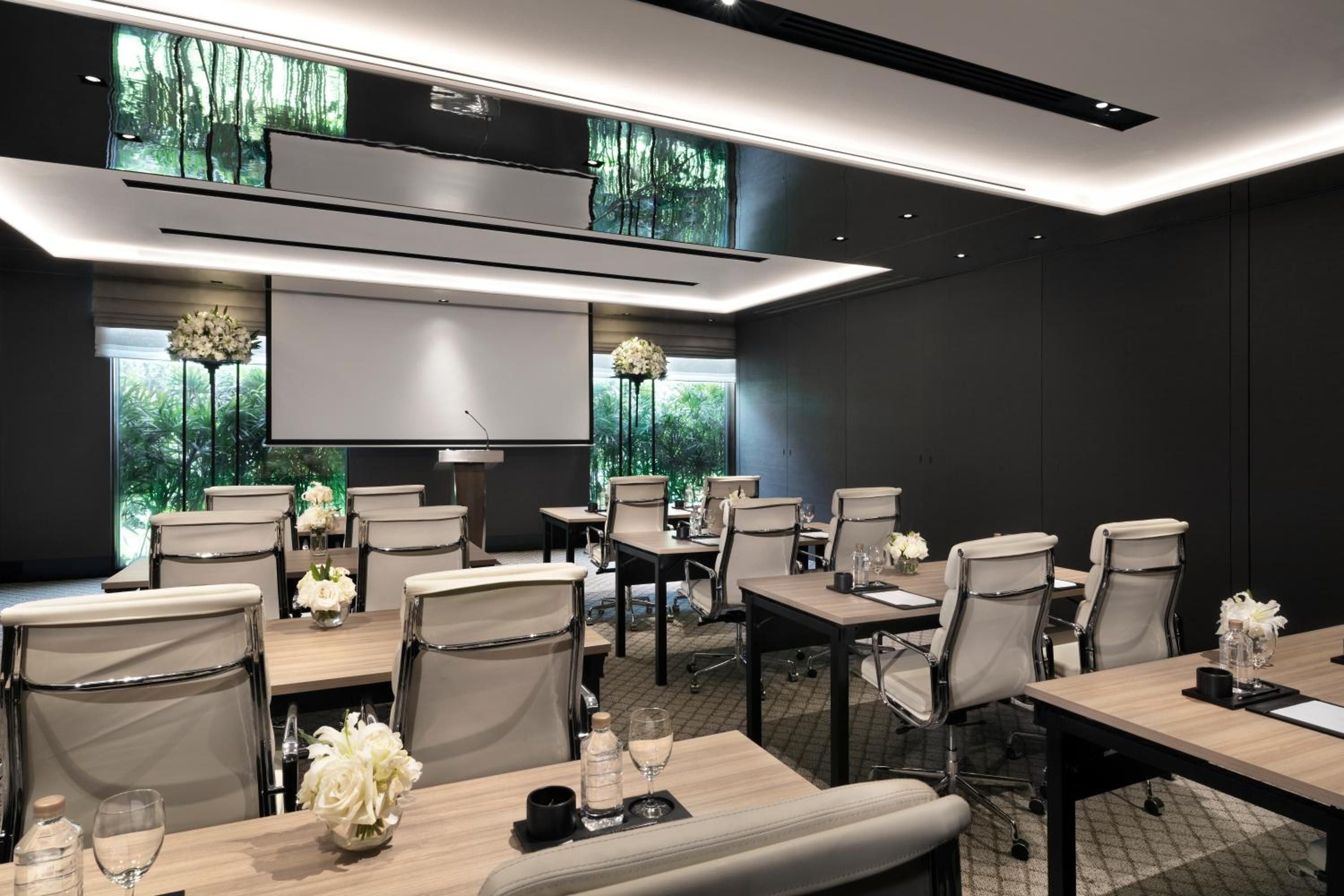 Sleek boardroom tables topped with crisp white orchids create an elegant atmosphere for gatherings, while floor-to-ceiling windows frame verdant tropical gardens beyond charcoal walls.