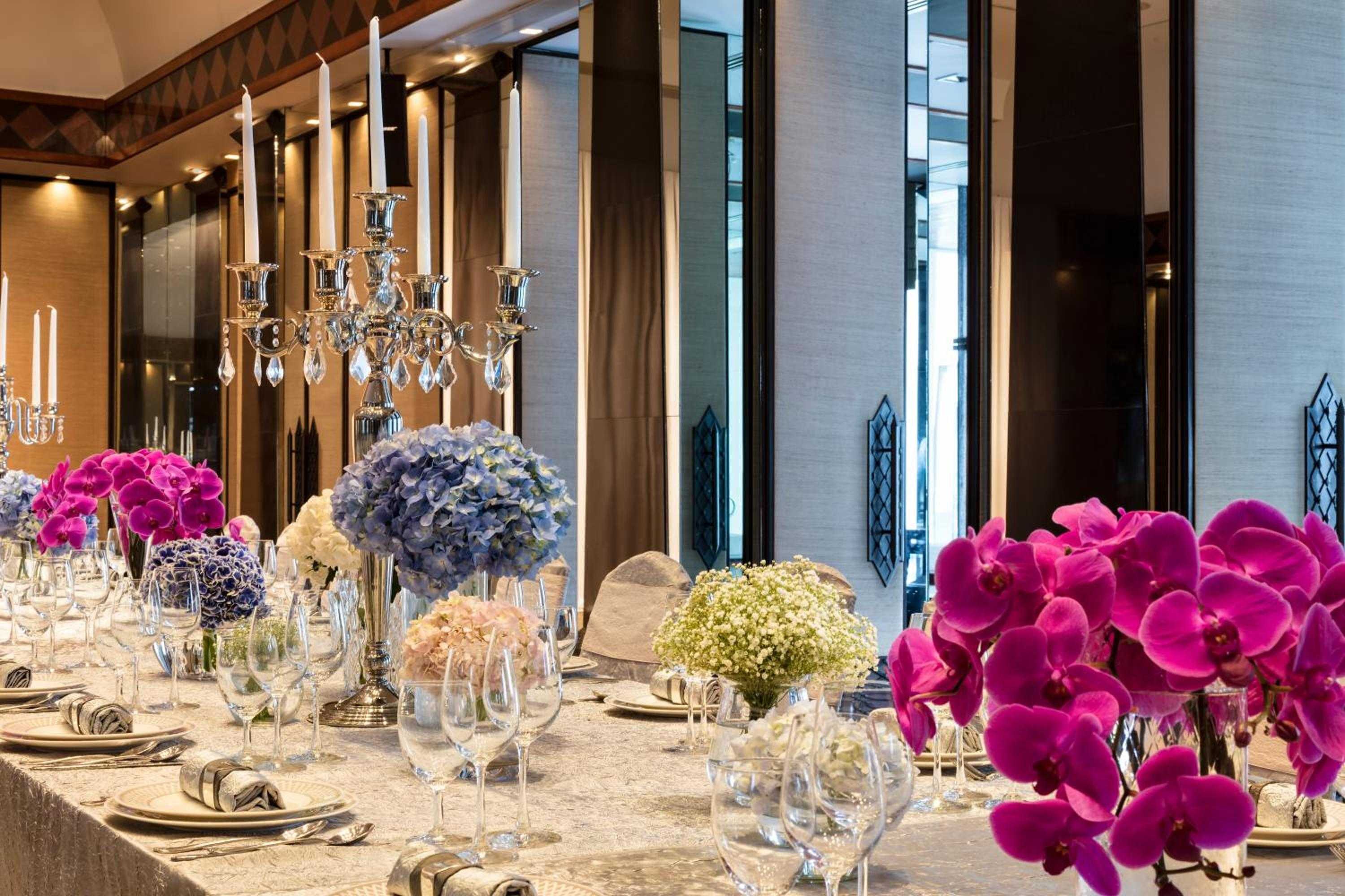 Crystal candelabras cast warm light over vibrant orchids and hydrangeas, where formal dining transforms into theatrical elegance through meticulous floral artistry and gleaming tableware.