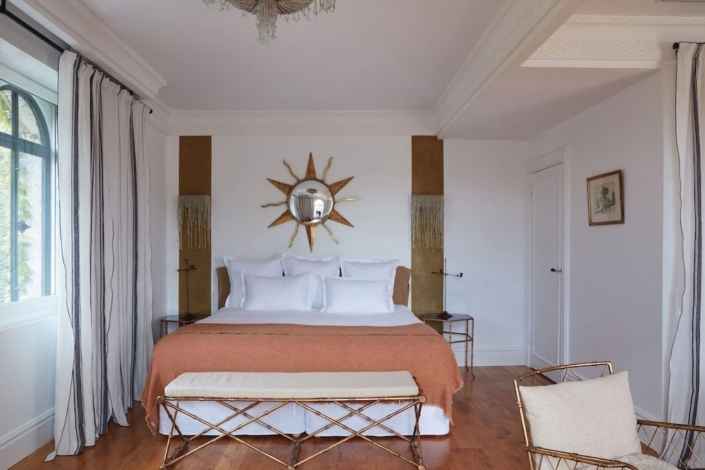 Crisp white linens contrast beautifully with coral throws in this sunlit guest room, where golden starburst mirrors and brass details create refined lakeside elegance.