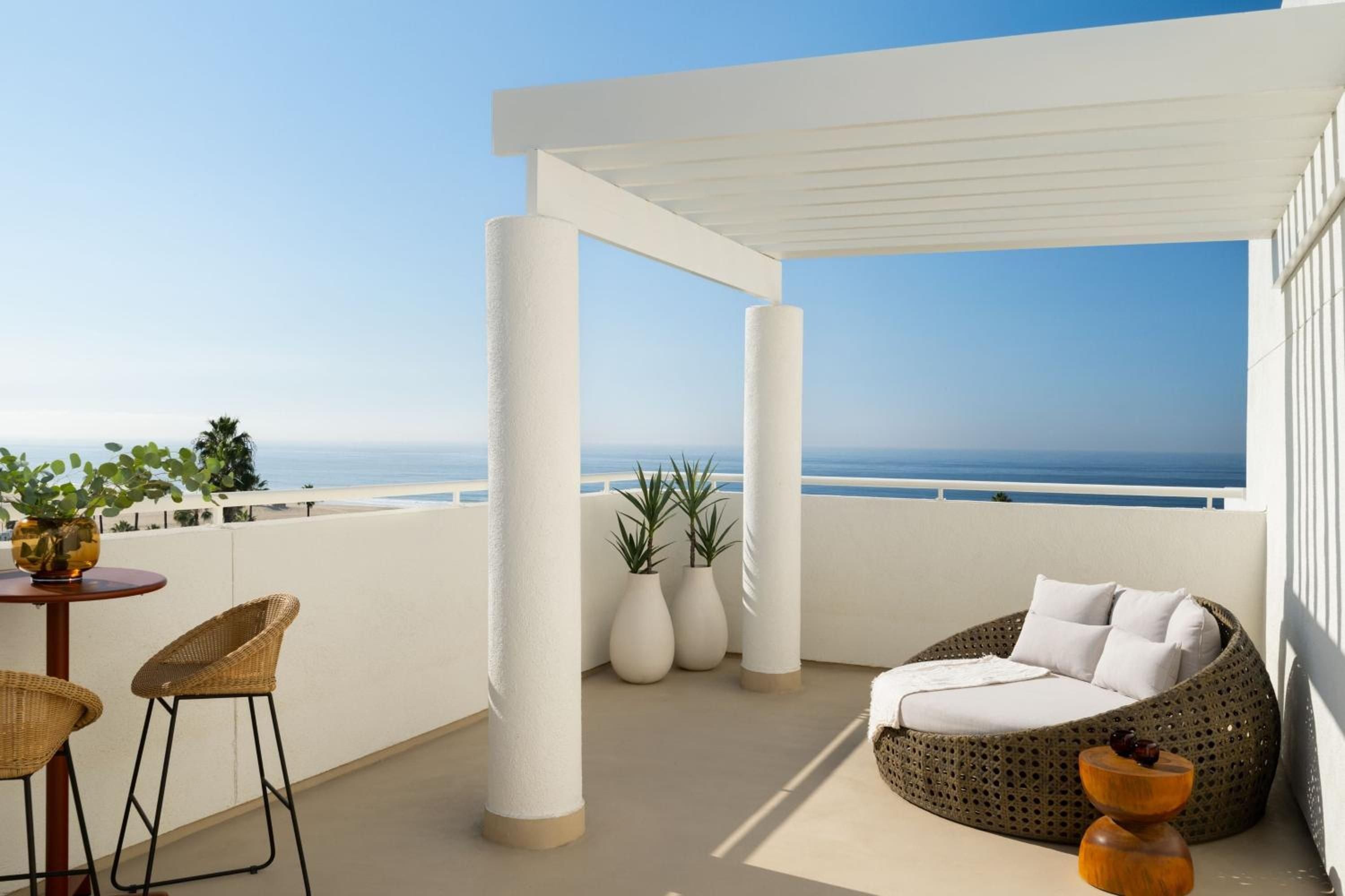 Wicker daybed and modern pergola frame endless Pacific views from this elevated terrace, where ceramic planters and amber glass accents catch the golden California light.