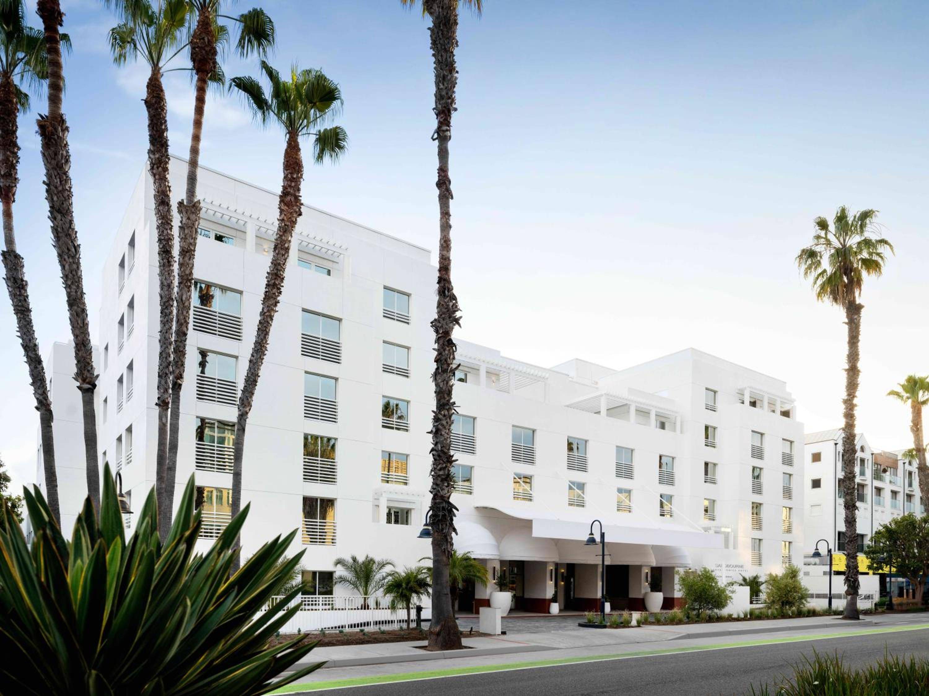 Palm trees frame the hotel's pristine white facade along Santa Monica's tree-lined streets, where modern architecture meets California's laid-back coastal charm.