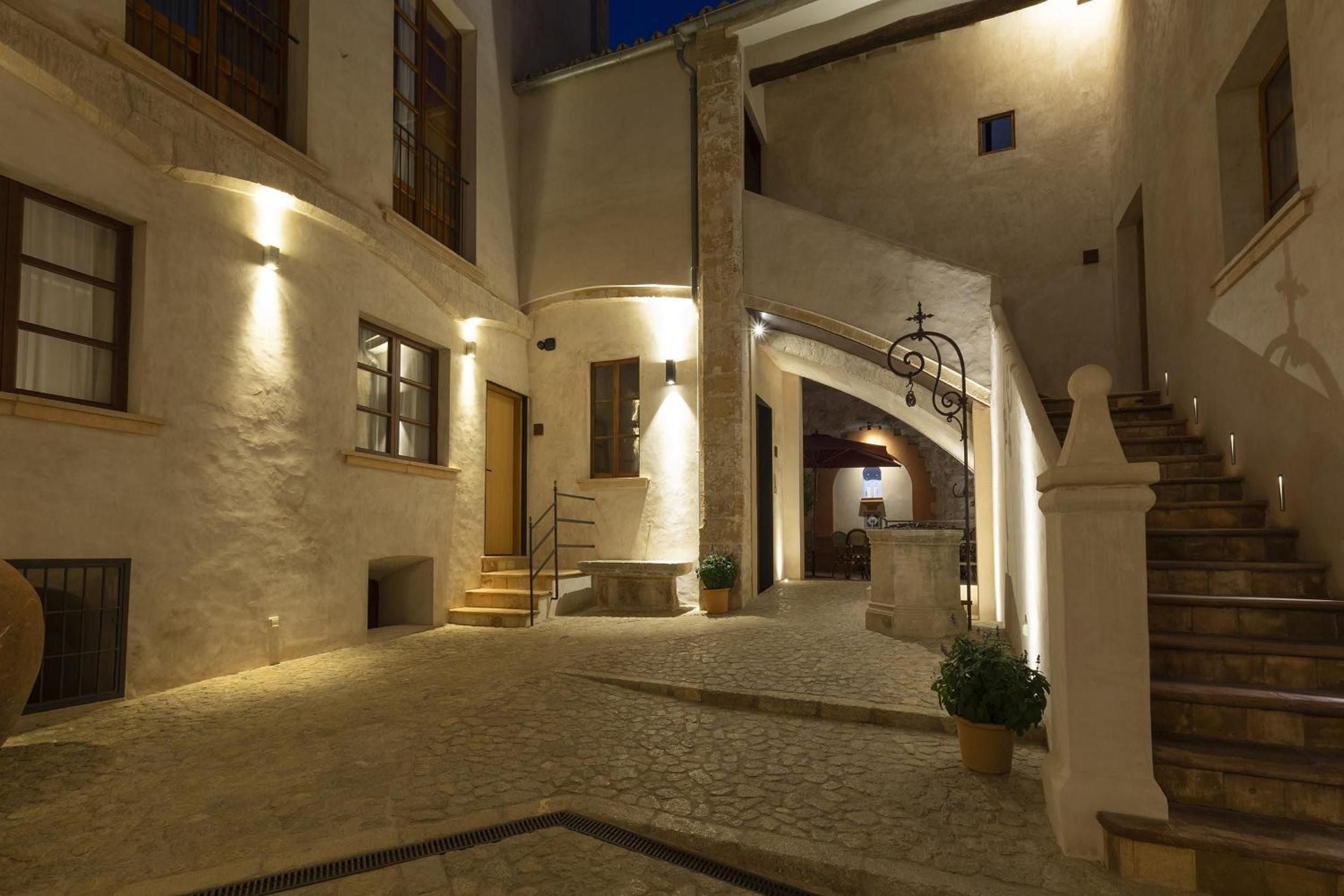 Honey-colored stone walls glow under subtle evening lighting in this intimate courtyard, where medieval architecture meets contemporary hospitality in perfect harmony.