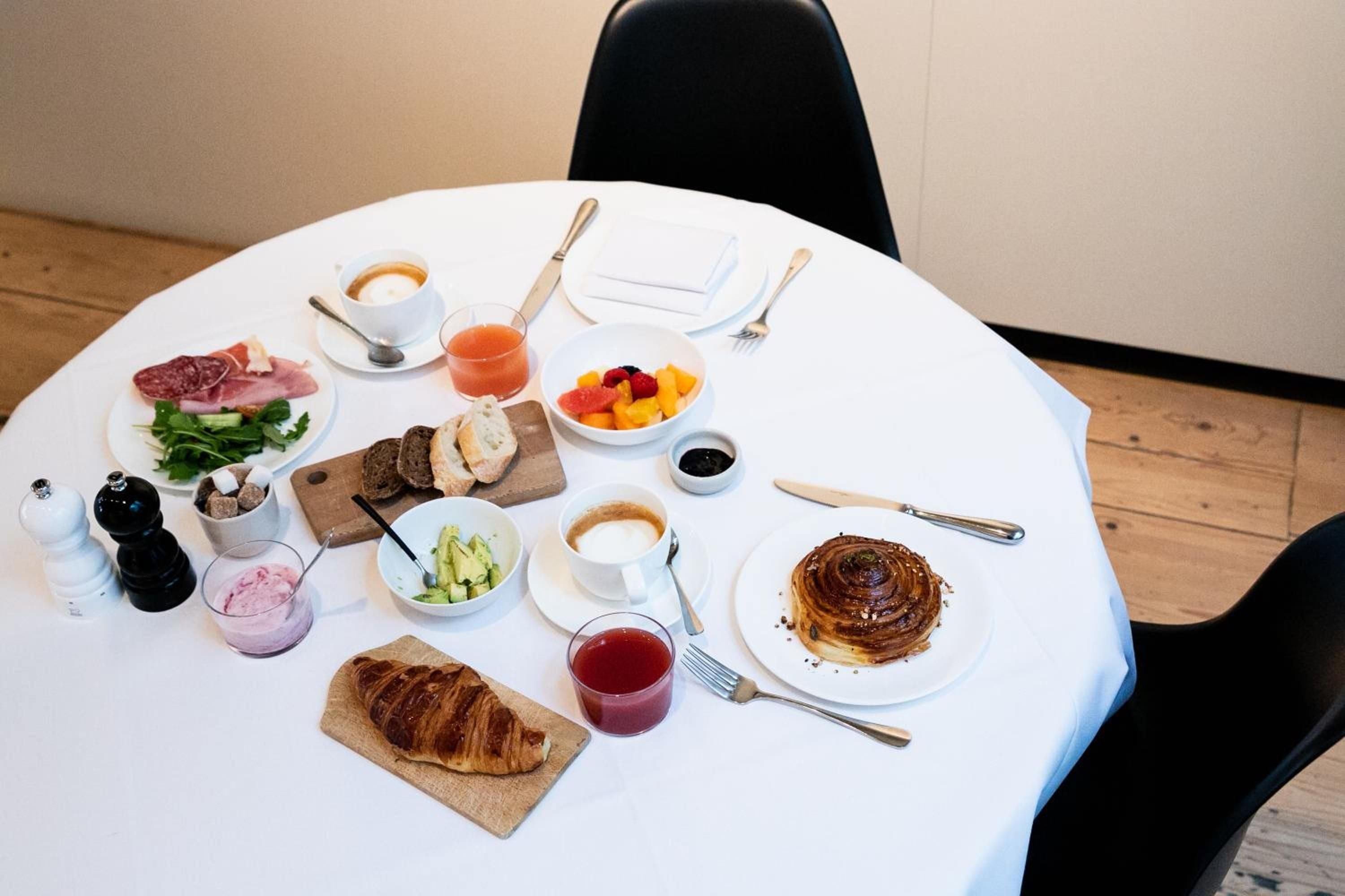 Artfully arranged breakfast spreads across crisp white linens—flaky croissants, vibrant fruit, and steaming coffee create an intimate morning ritual in this thoughtfully curated dining experience.
