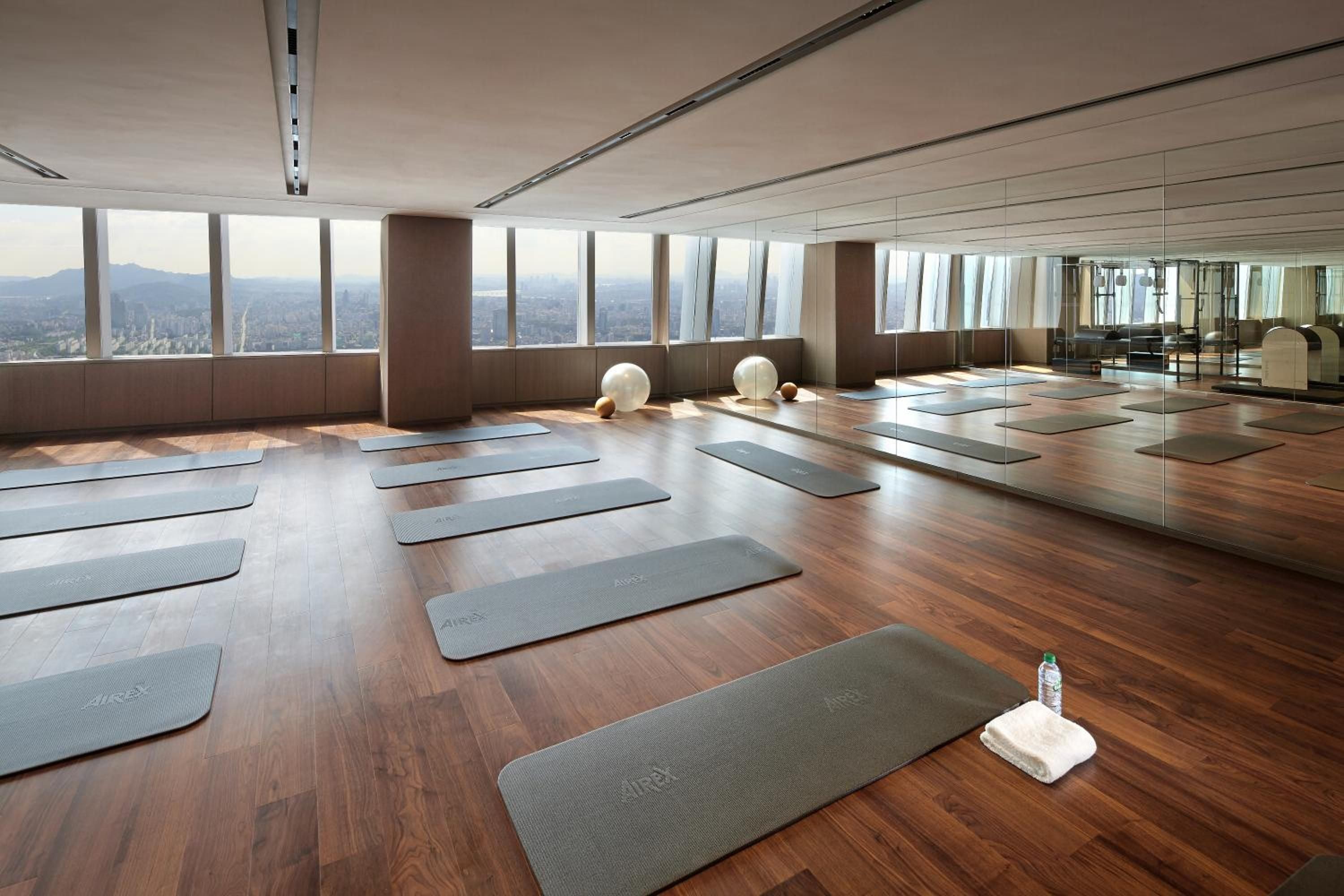 Floor-to-ceiling windows frame Seoul's skyline while yoga mats await practice sessions in this serene studio, where polished hardwood floors reflect natural light streaming across the space.