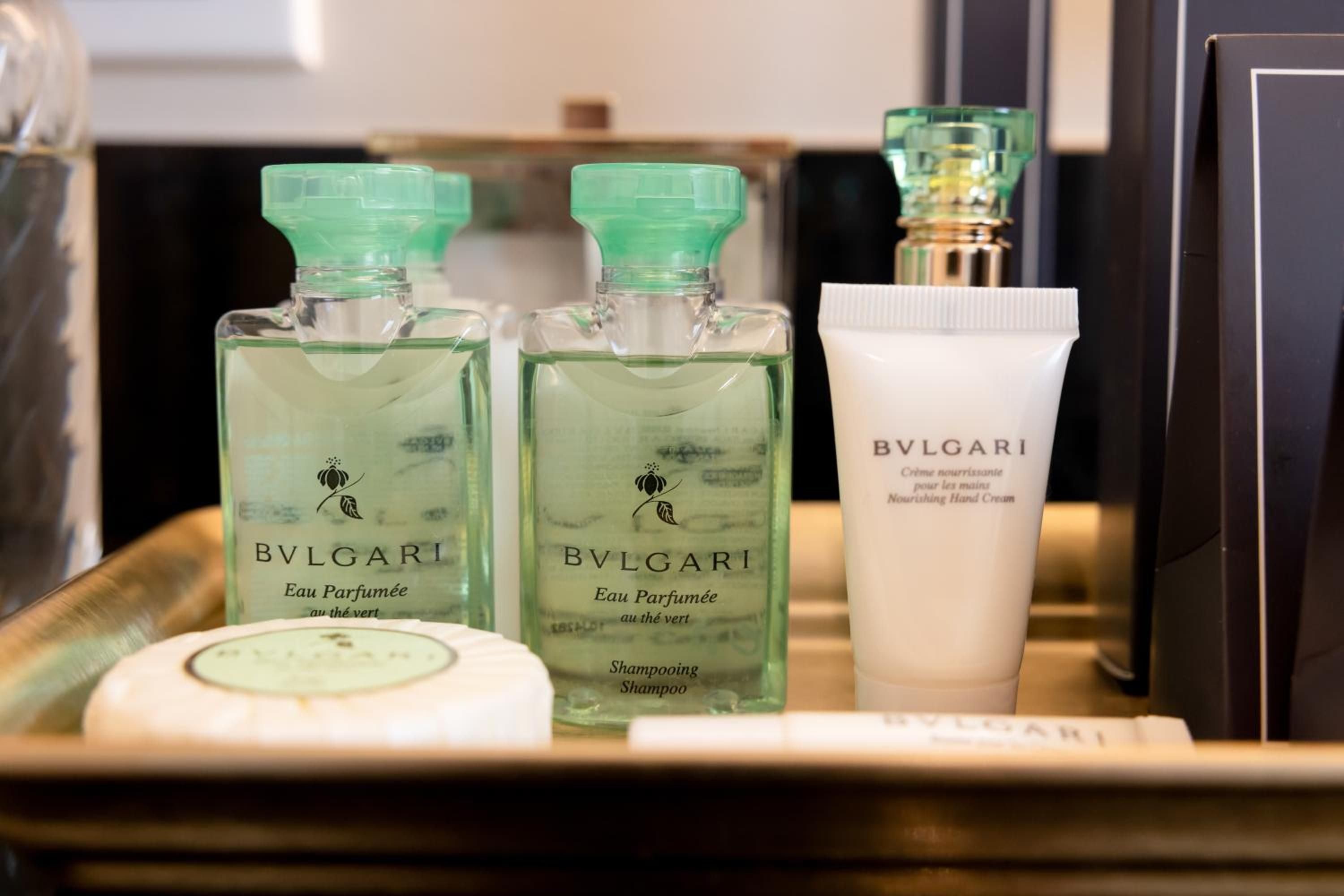 Bulgari's signature green tea amenities grace marble surfaces, transforming daily rituals into moments of Italian luxury with perfumed shampoos and nourishing hand cream.