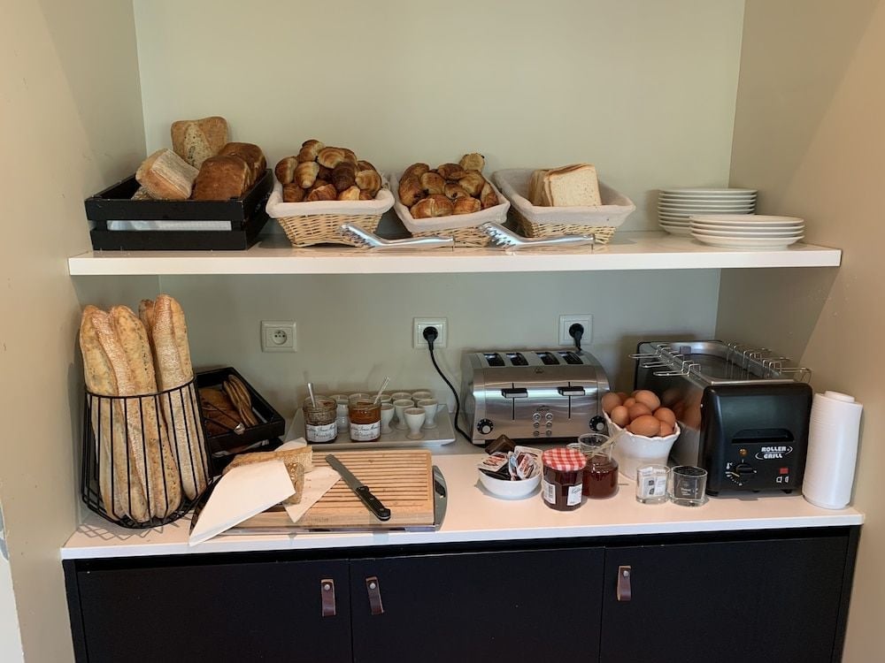 Fresh baguettes stand sentinel in wire baskets while artisanal jams and a gleaming toaster promise leisurely mornings at this thoughtfully curated breakfast station.