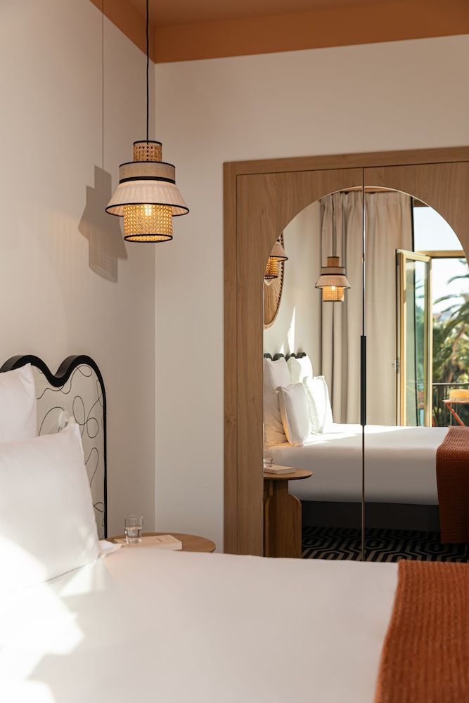 Woven pendant lights cast warm shadows across crisp linens, while the curved mirror reflects intimate corners where natural textures meet contemporary French design.