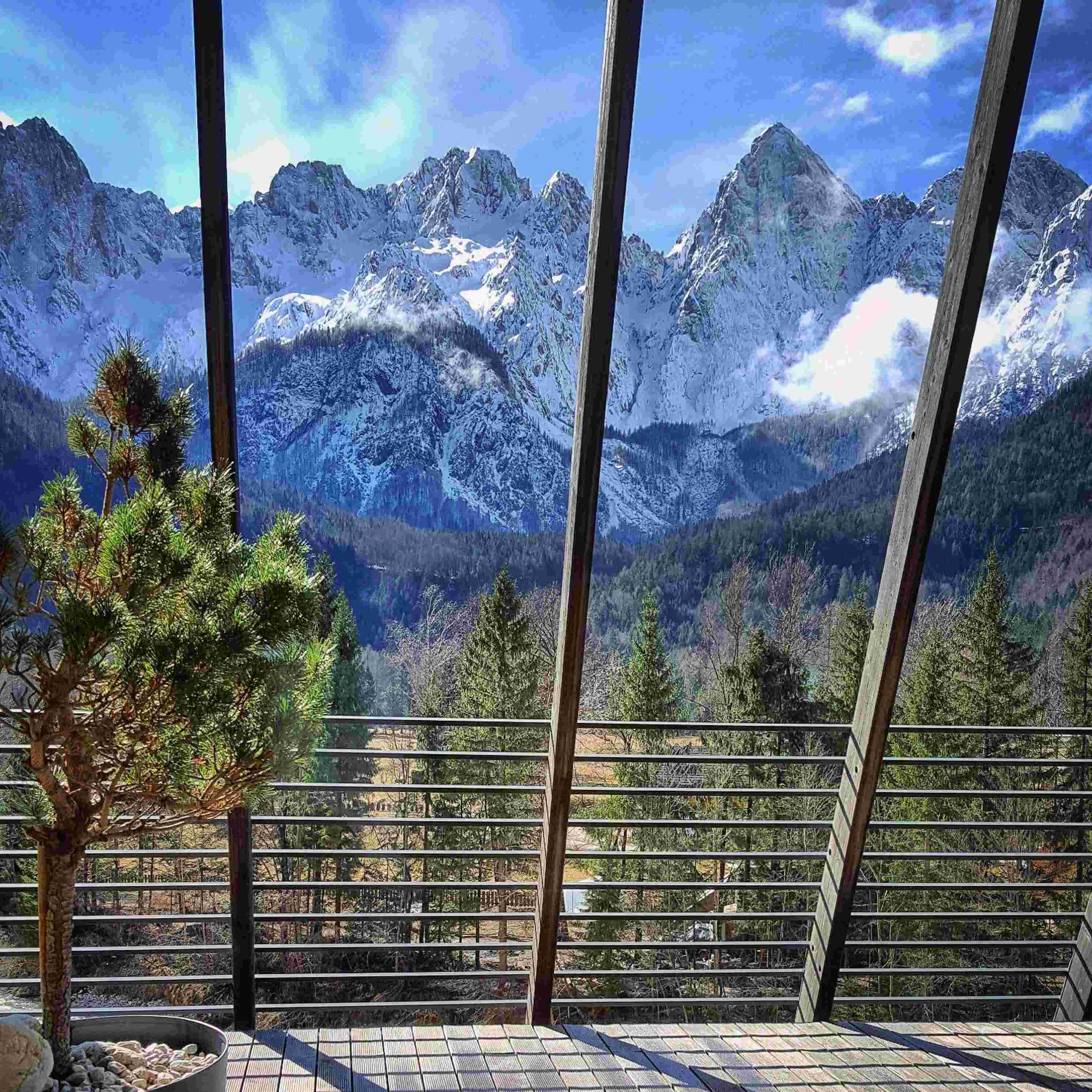 Snow-dusted Julian Alps frame this contemporary terrace, where horizontal railings and geometric tiles create striking contrast against the dramatic limestone peaks beyond.