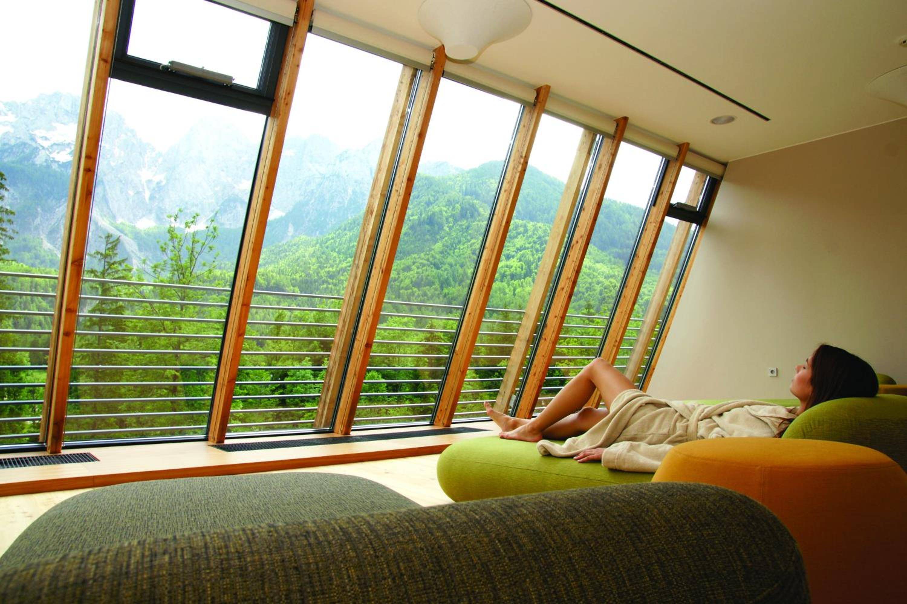 Angled windows frame emerald Alpine valleys as guests unwind on heated loungers, where warm wood and mountain air create perfect sanctuary moments.