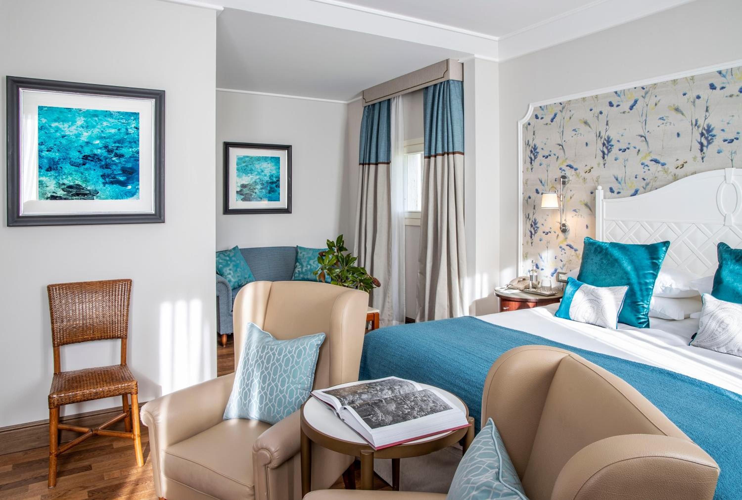 Aqua accents and botanical wallpaper create a serene retreat where plush armchairs invite lingering over coffee while Mediterranean light filters through layered curtains.