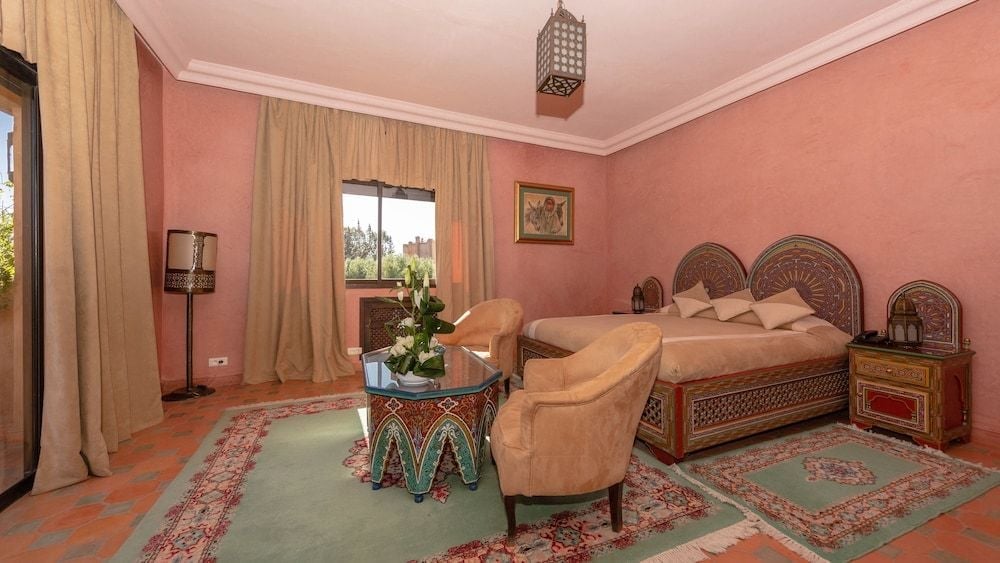 Ornate carved headboards and intricate metalwork tables create an authentic Moroccan sanctuary, where warm terracotta walls glow softly in the Atlas Mountain light.