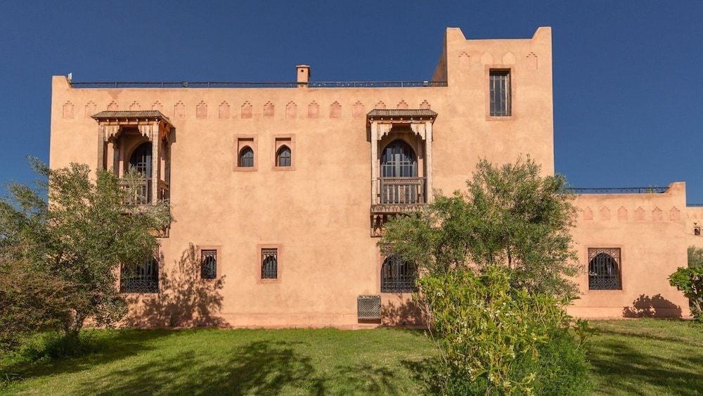 Adobe walls glow like burnished copper against cerulean skies, while carved wooden balconies and manicured gardens create an oasis of Moroccan elegance.