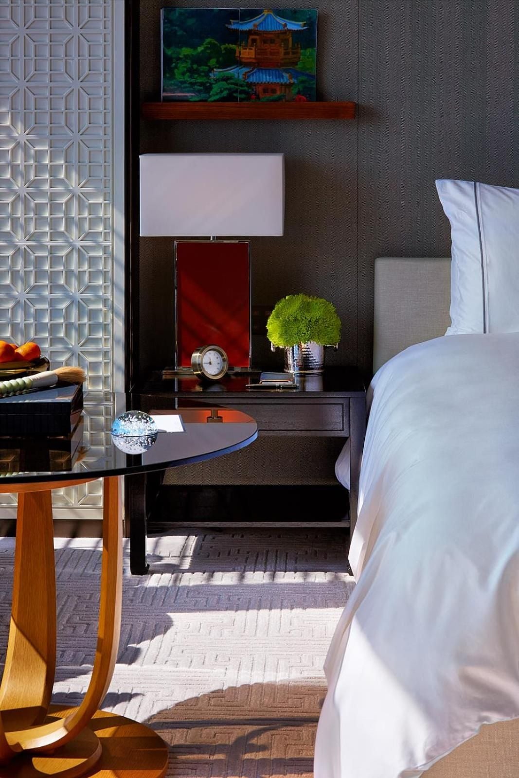 Crisp white linens meet dark wood furnishings in thoughtfully appointed guest rooms, where geometric screens filter natural light across handwoven rugs and carefully curated Asian art.