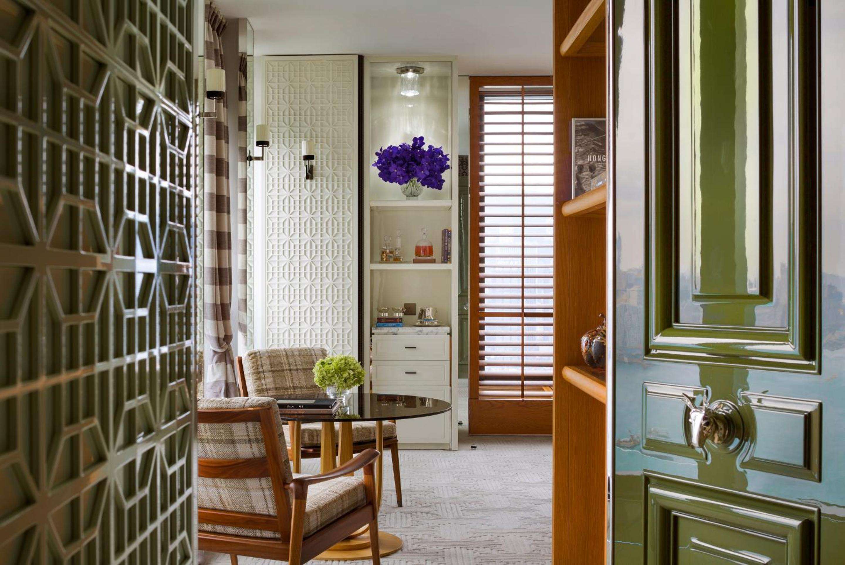 Jade-green doors open onto a sophisticated sitting area where geometric screens filter natural light across plush armchairs and carefully curated shelving.