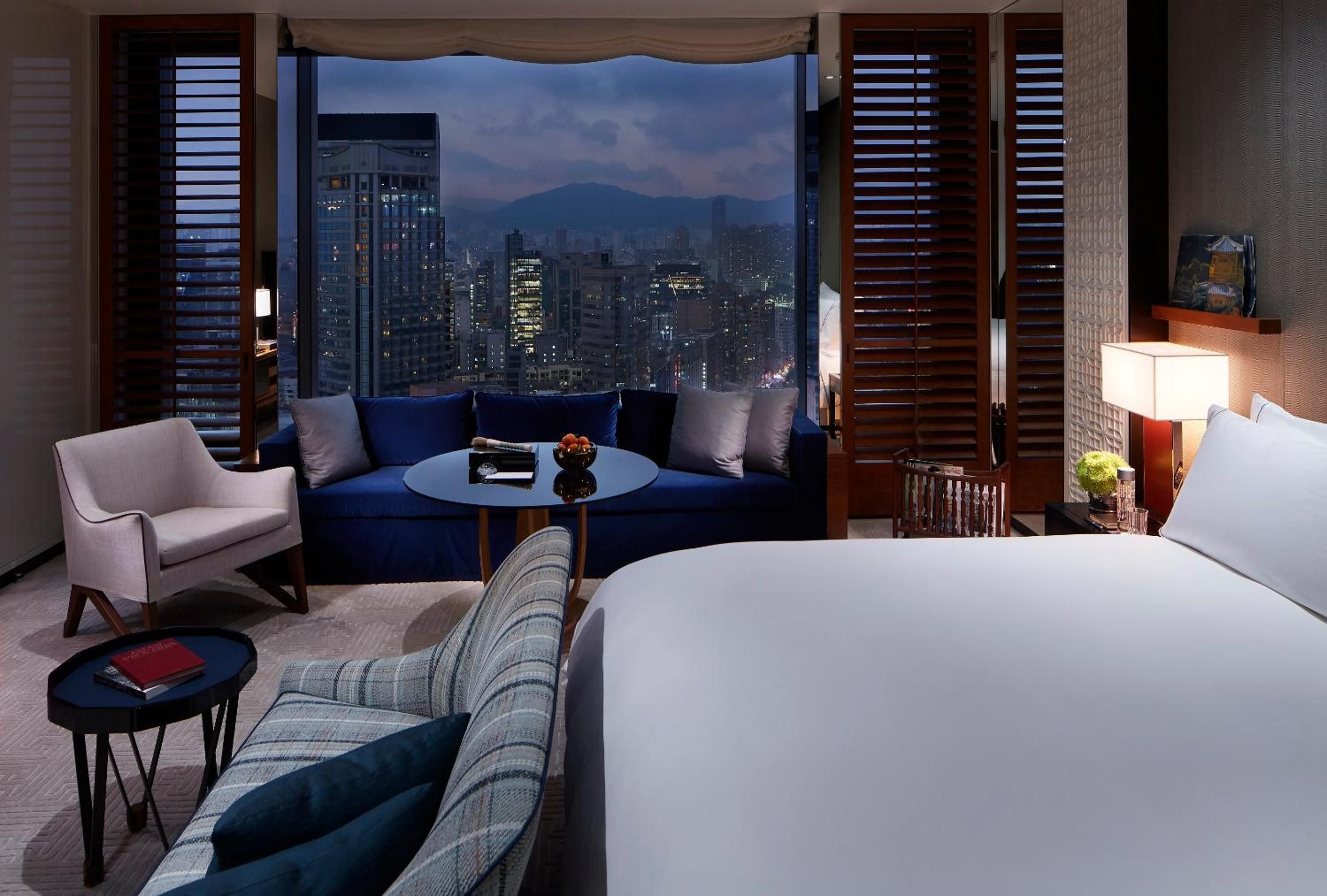 Floor-to-ceiling windows frame Victoria Harbour's glittering skyline while plush navy seating and warm wood shutters create an intimate sanctuary above the city's pulse.