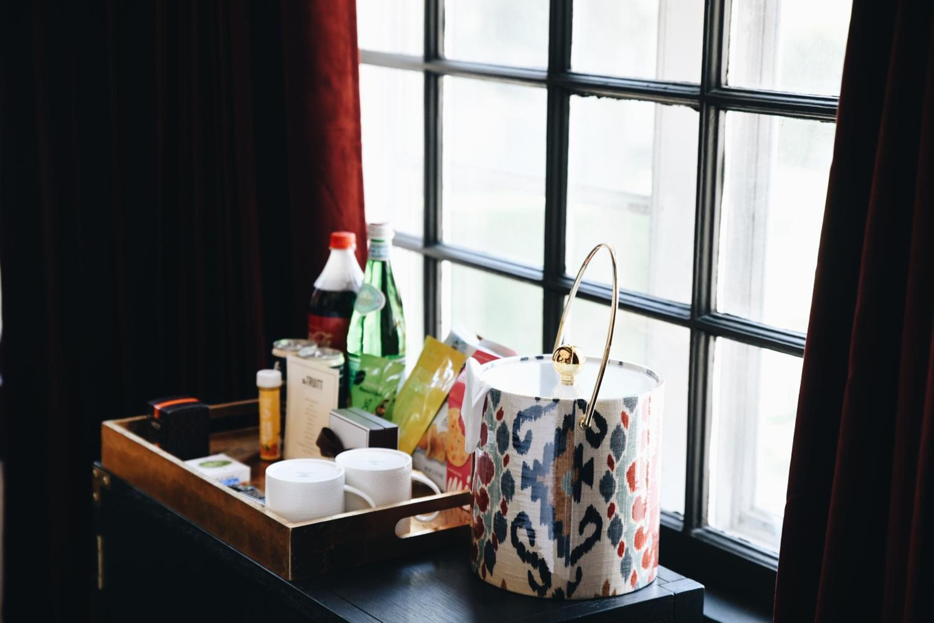 Afternoon light streams across a curated collection of artisanal bottles and patterned textiles, where brass handles catch the glow from mullioned windows.
