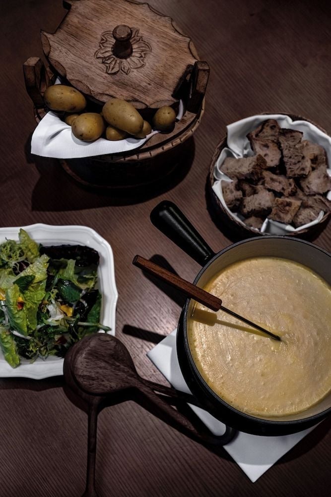 Rustic wooden vessels cradle golden potatoes while molten cheese fondue bubbles in cast iron, embodying the chalet's commitment to Alpine comfort and conviviality.