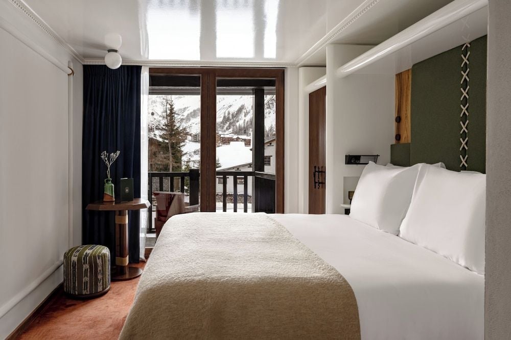 Alpine serenity unfolds beyond floor-to-ceiling windows, where crisp white linens and sage green accents create a cocoon against Val d'Isère's snow-dusted peaks.