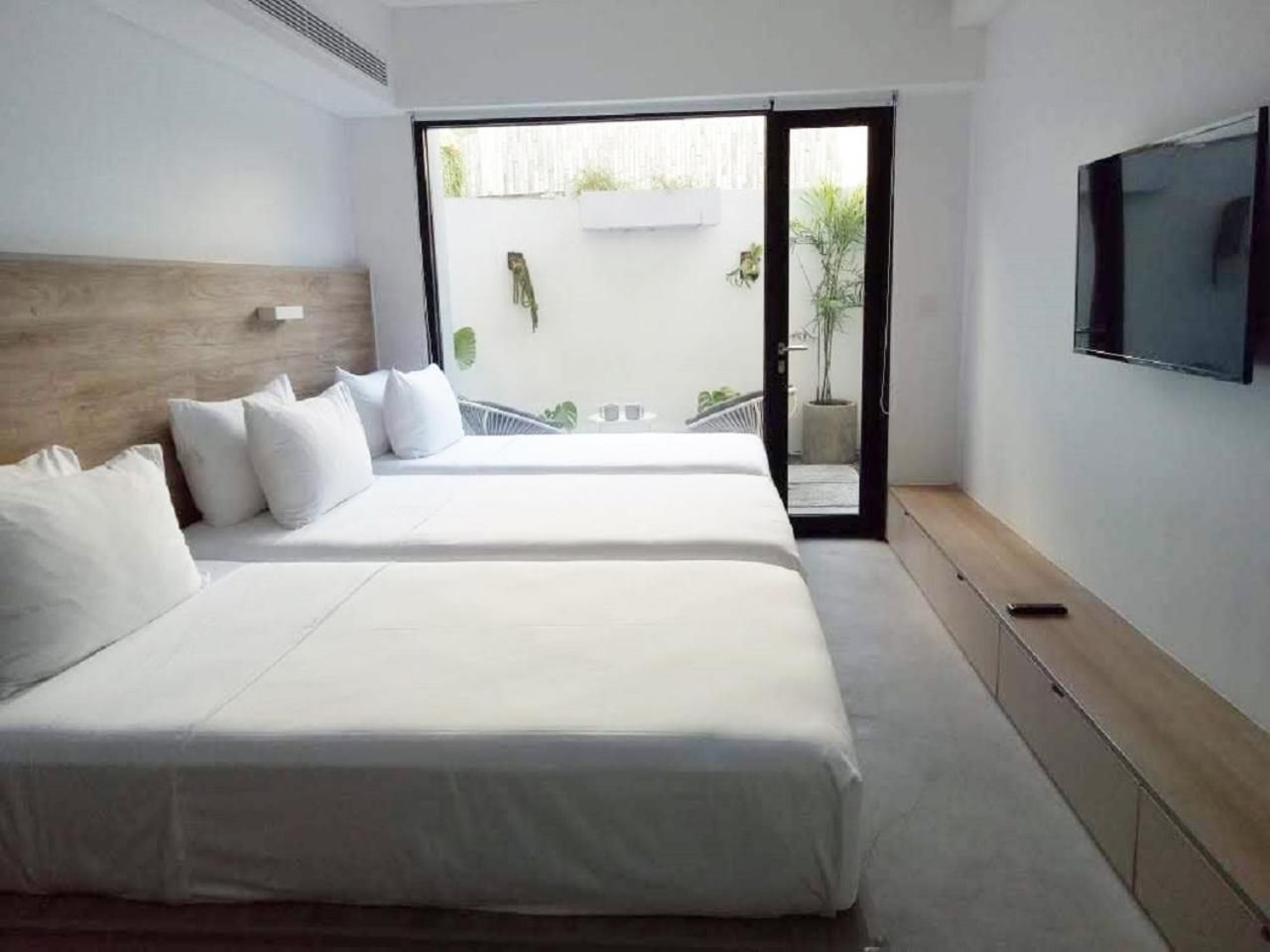 Crisp white linens meet warm wood accents in this serene twin room, where floor-to-ceiling windows frame a private terrace dotted with tropical greenery.