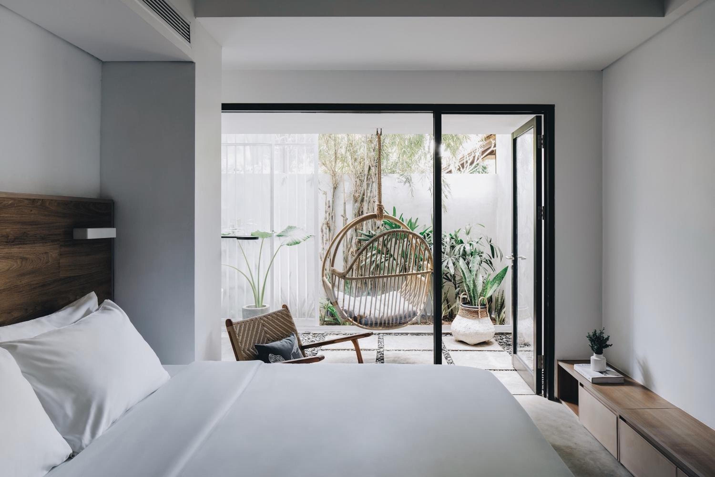 Crisp white linens frame views of a private terrace where a suspended rattan chair beckons beneath swaying palms and dappled tropical light.