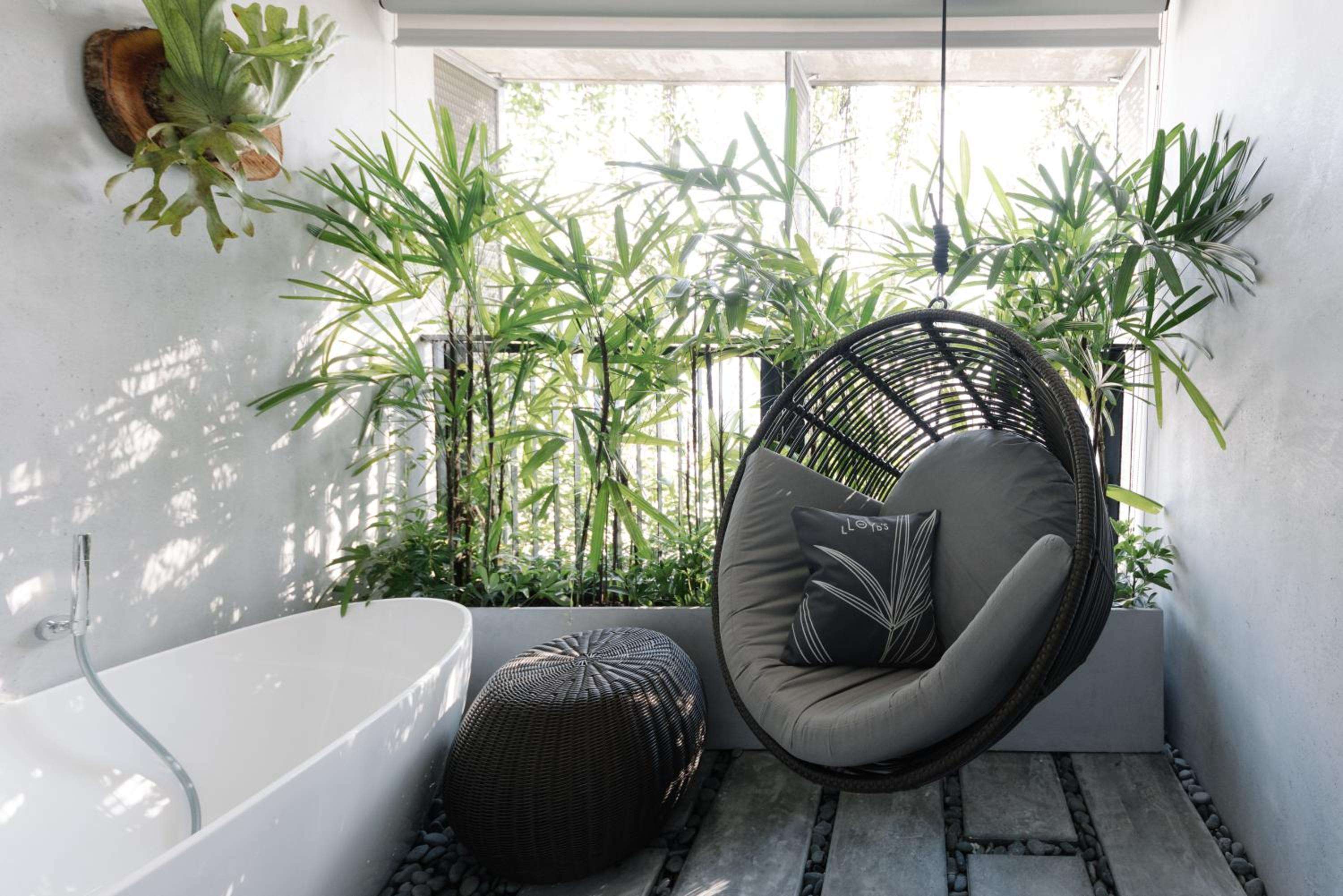 Natural light filters through frosted windows onto sleek wicker furnishings and a sculptural soaking tub, while lush palms transform this bathroom into a tropical sanctuary.