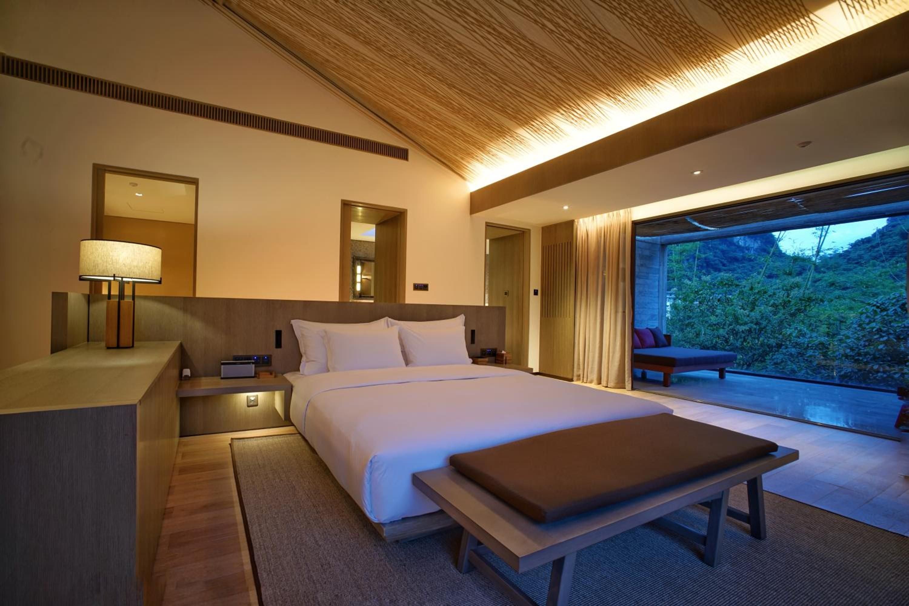 Warm bamboo ceilings and integrated lighting create an intimate sanctuary where floor-to-ceiling windows blur the boundary between luxurious interiors and lush tropical gardens.