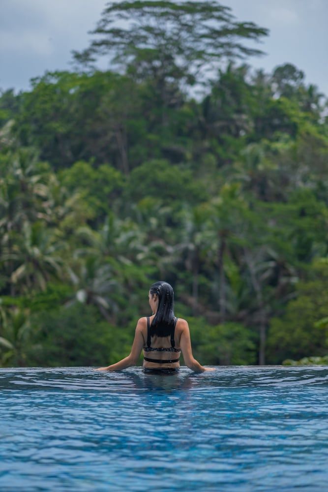 Infinity waters blend seamlessly with Bali's emerald jungle canopy as guests float in serene contemplation, cocooned by tropical tranquility at this intimate hillside retreat.