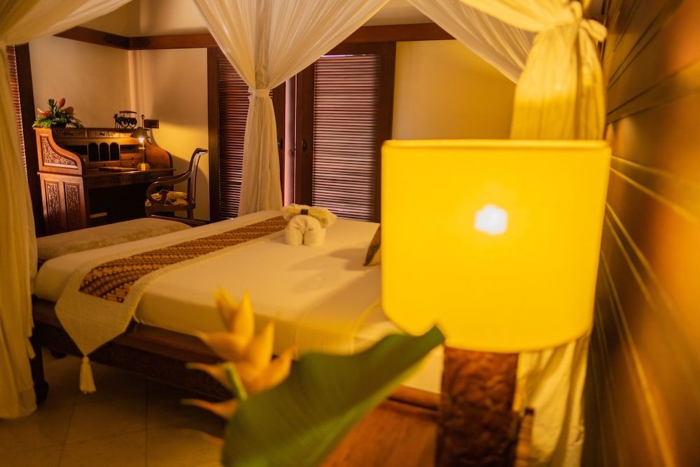 Warm amber light bathes the canopy bed while a laptop glows softly, blending modern connectivity with traditional Balinese romance in this intimate suite.