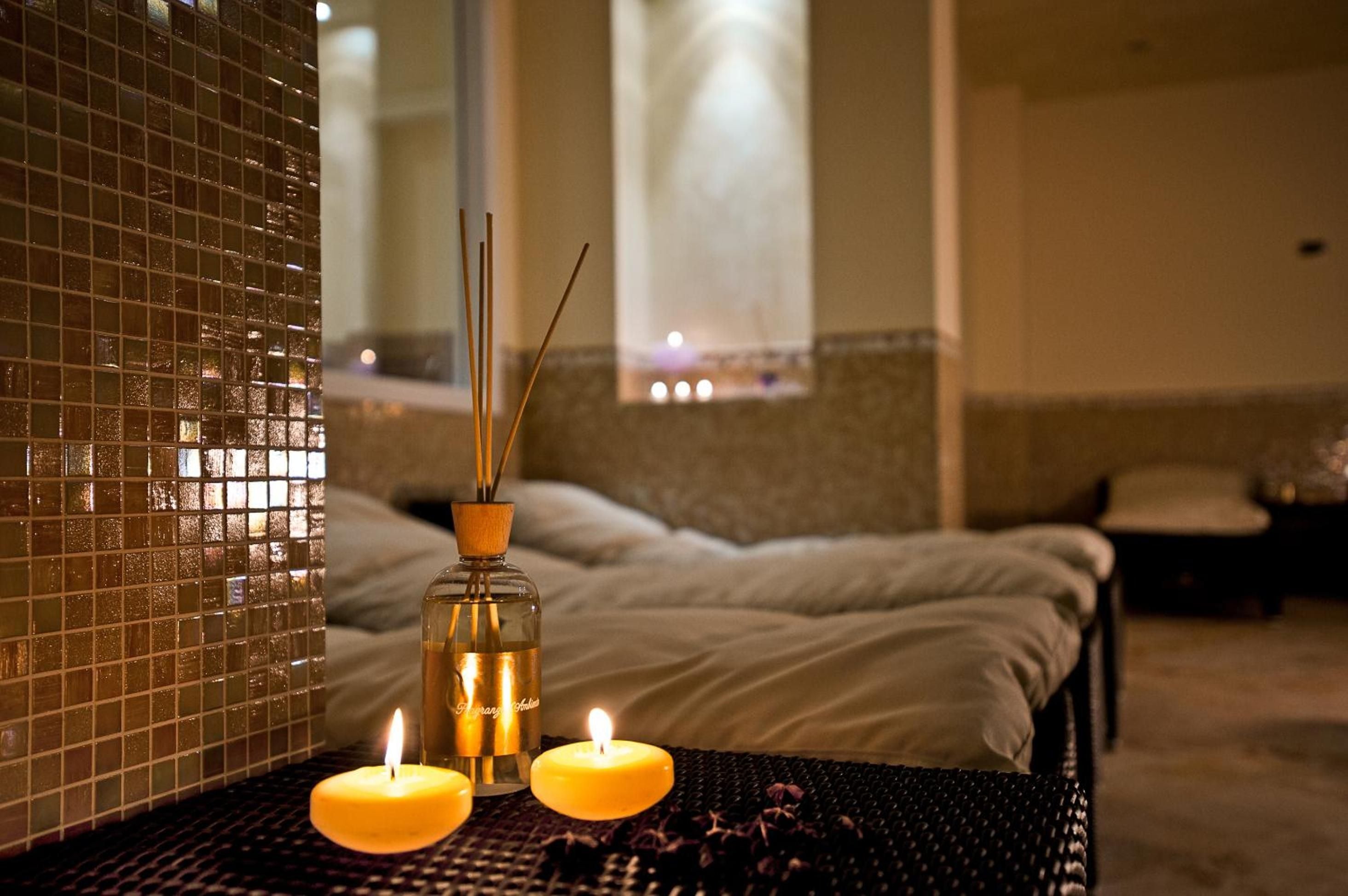 Reed diffusers and floating candles cast amber light across mosaic tiles, creating an intimate sanctuary where therapeutic treatments unfold in serene luxury.