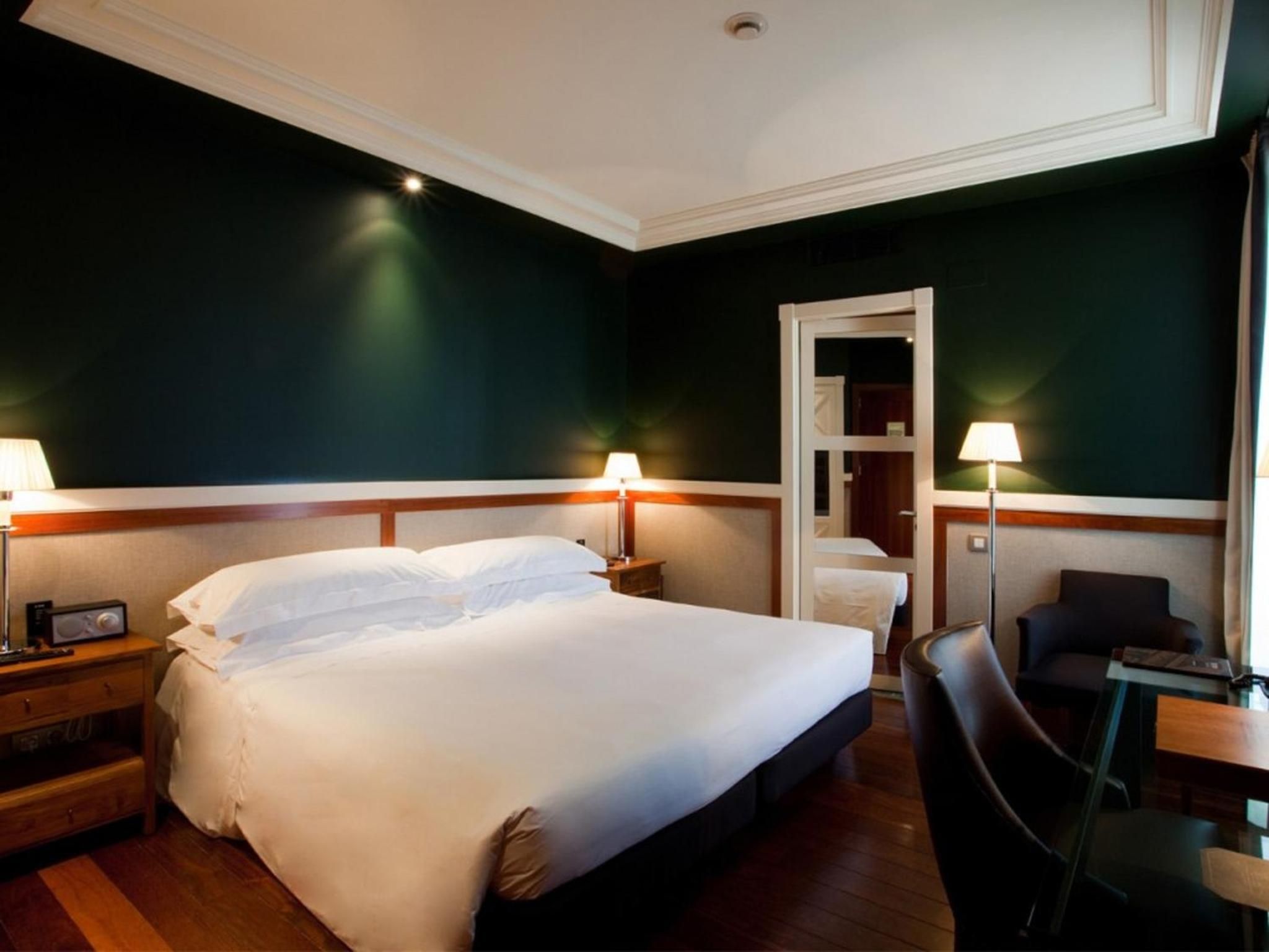 Emerald walls and warm wood create an intimate sanctuary, where crisp white linens invite rest beneath the gentle glow of bedside lamps.