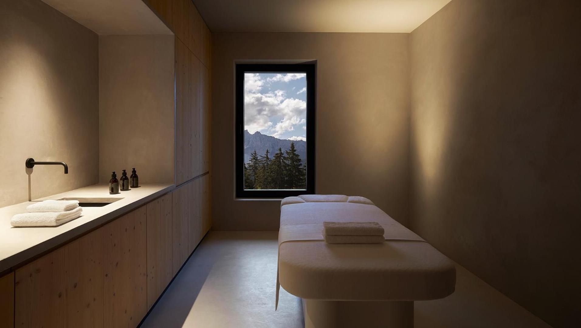 Alpine vistas frame this serene treatment room where warm wood meets creamy limestone, creating an intimate sanctuary for mountain-inspired wellness rituals.