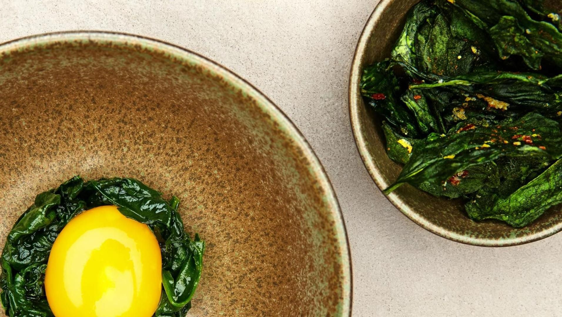 Handcrafted ceramic bowls cradle vibrant spinach and golden egg yolk, showcasing the Alpine resort's farm-to-table philosophy through artful presentation and earthy textures.