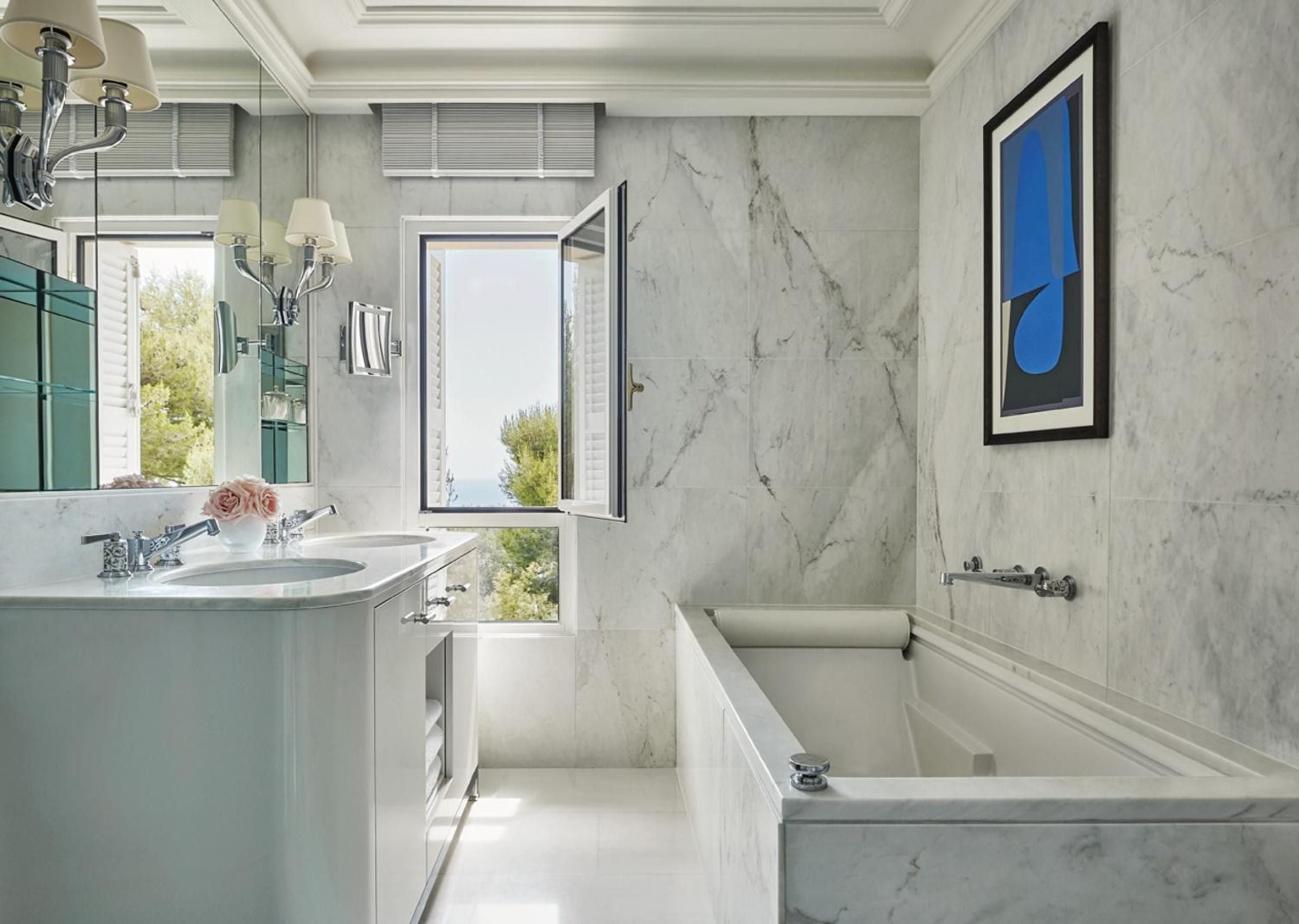Carrara marble envelops this palatial suite bathroom, where French windows frame Mediterranean views and modern luxury meets timeless Riviera elegance.