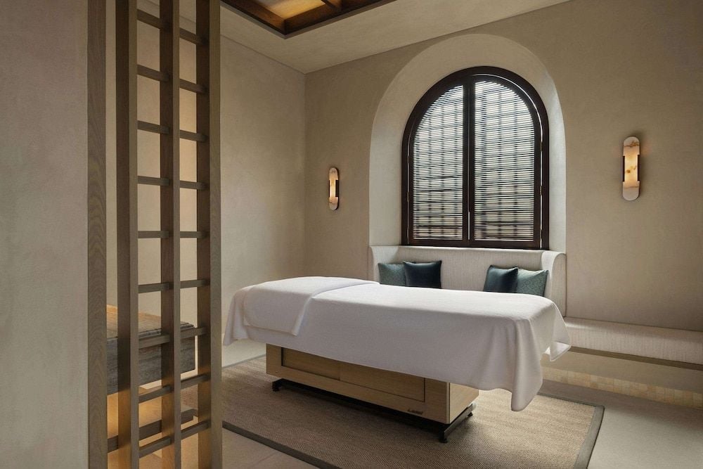 Serene treatment room combines Moorish archways with contemporary minimalism, where warm stone walls and filtered light through woven blinds create a sanctuary for renewal.