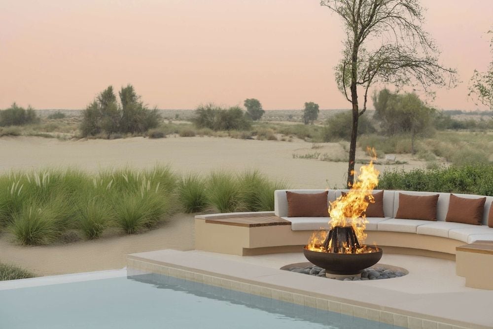 Desert winds whisper through native grasses as flames dance in the fire bowl, while curved seating overlooks endless dunes painted rose-gold by twilight.