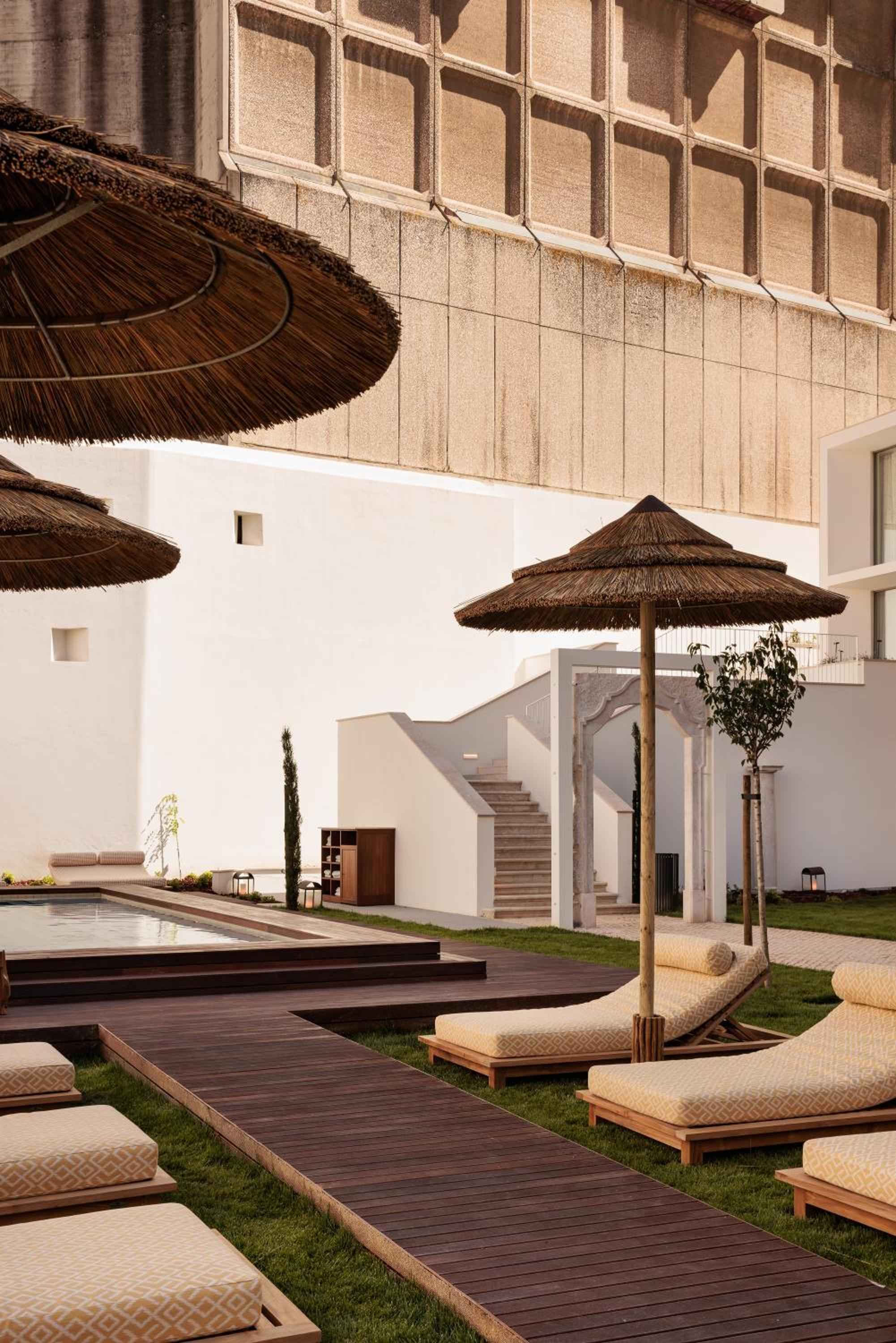 Thatched umbrellas cast dappled shadows over honey-colored loungers, where weathered stone meets sleek decking in this serene poolside sanctuary.