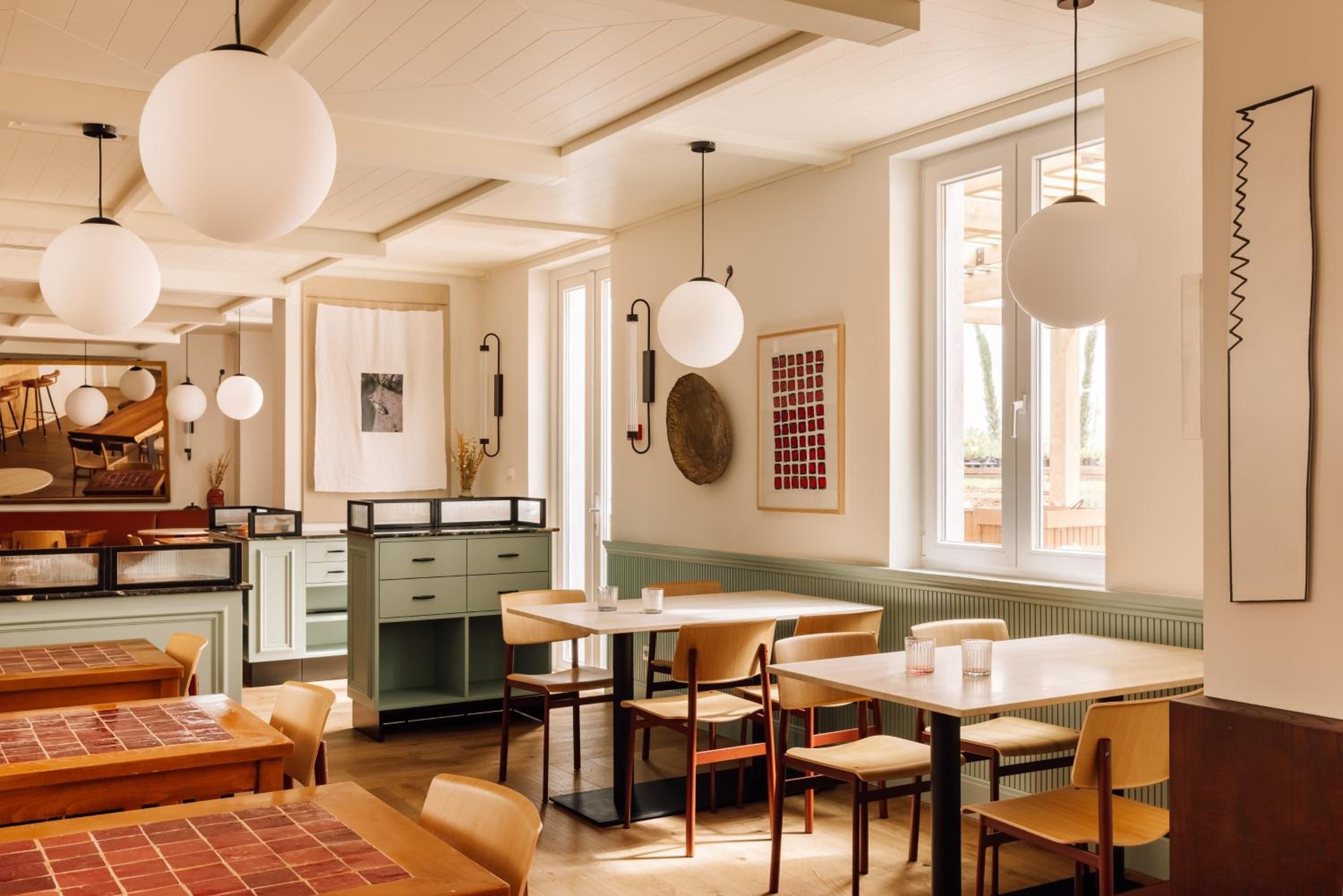 Sage-green wainscoting and warm pendant lighting create an inviting communal dining space where Scandinavian-inspired furniture meets Portuguese charm in perfect harmony.
