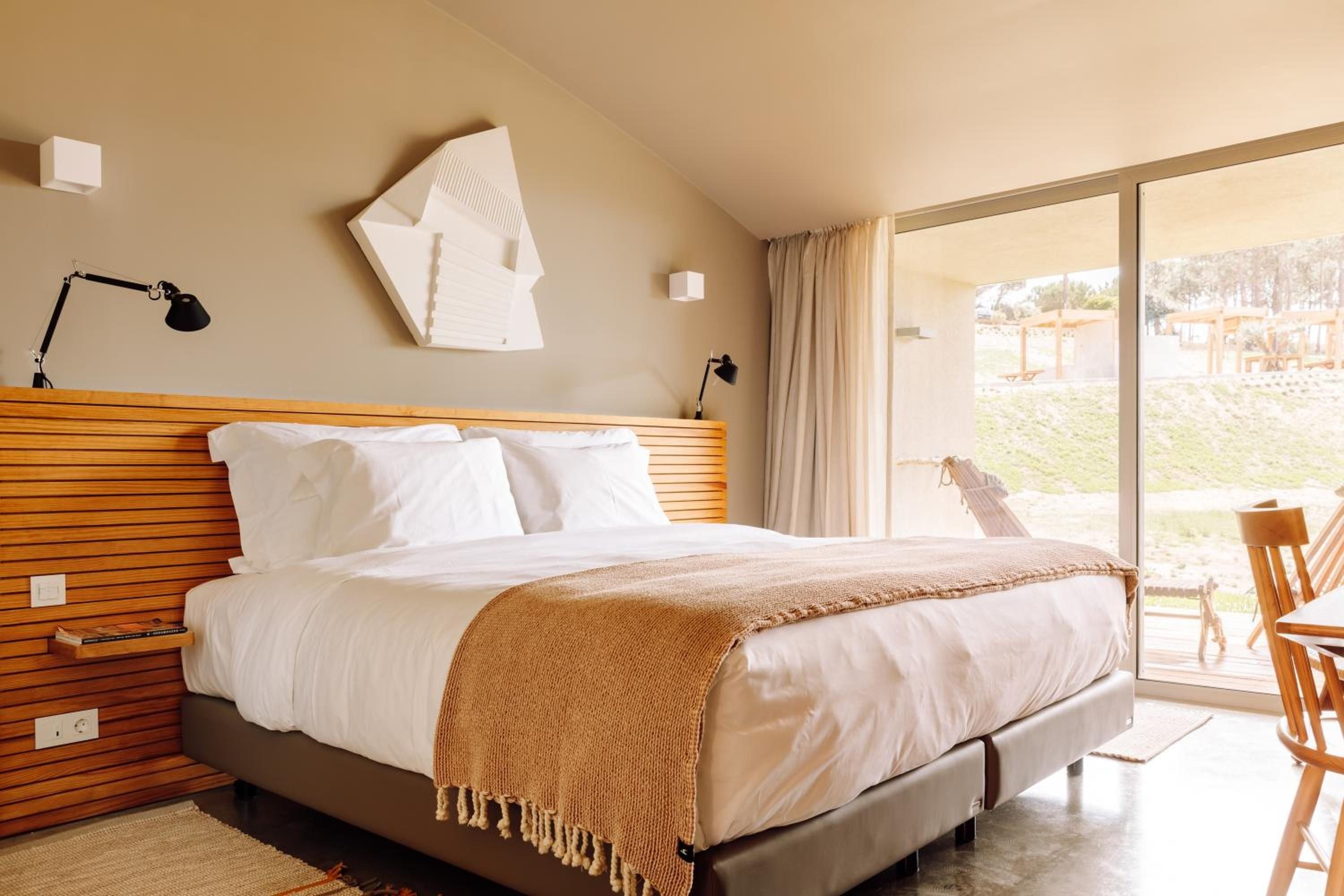 Warm wood slats frame the platform bed while natural light floods through floor-to-ceiling windows, creating an effortlessly modern sanctuary with earthy textures.